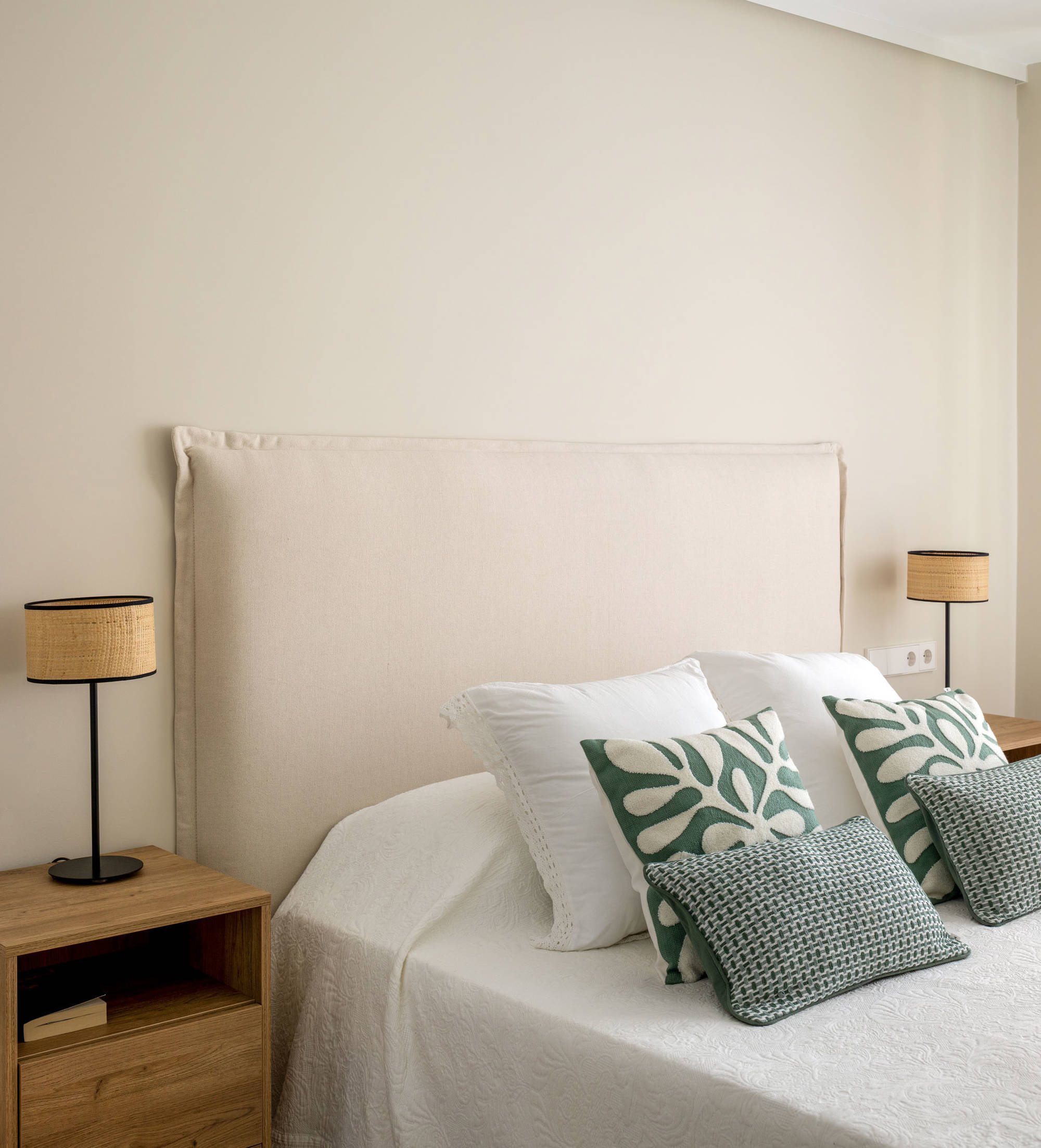 Dormitorio con mesitas de madera, cabecero tapizado y cojines verdes.