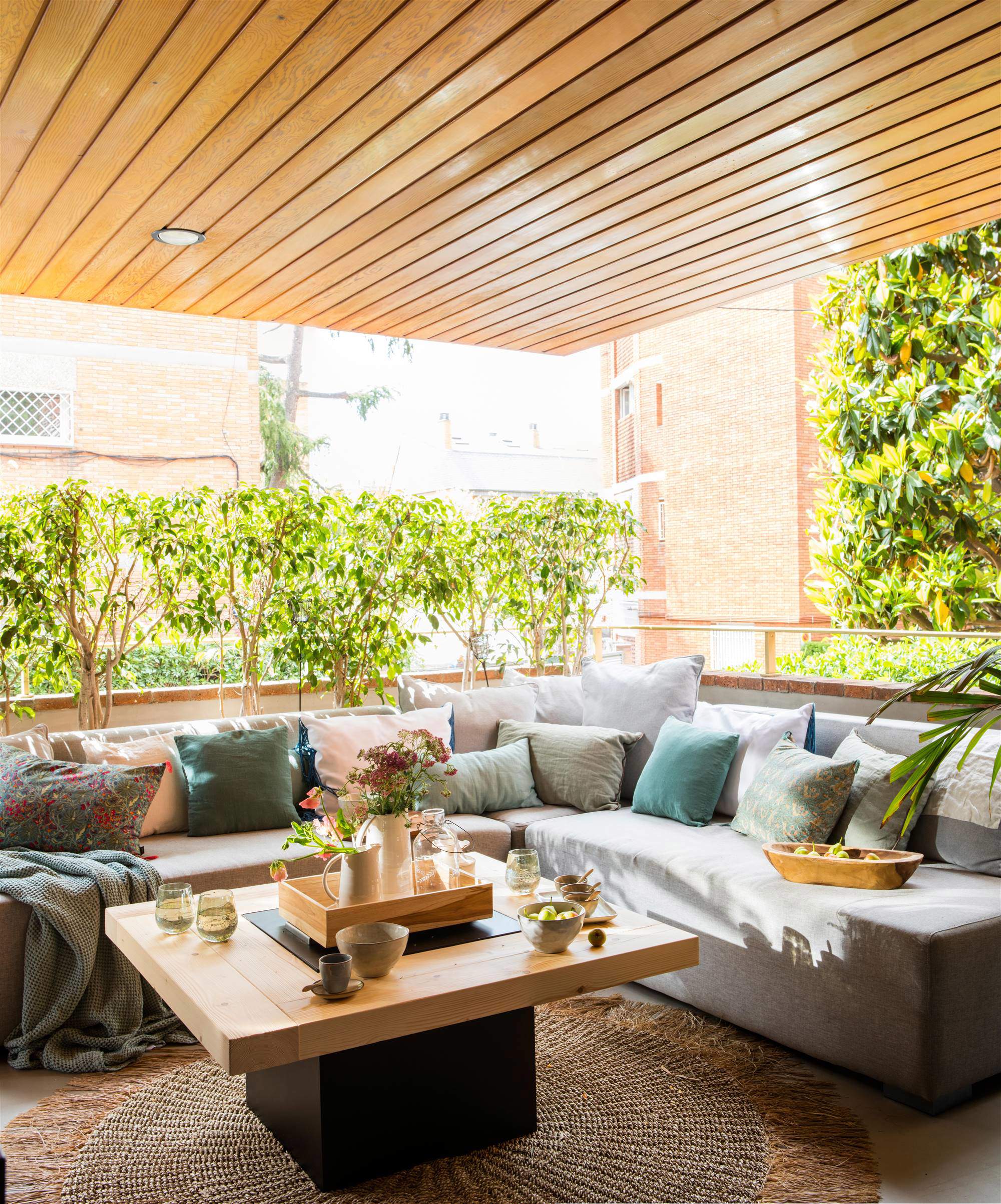 Terraza con encanto con sofá en L a medida, mesa de madera y árboles altos 00543390