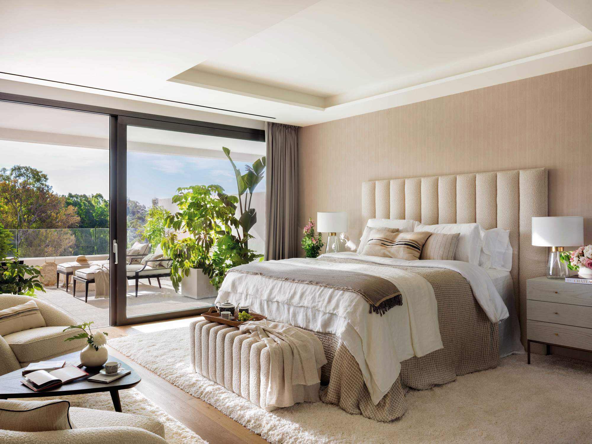 Dormitorio de matrimonio moderno con cama alta y cabecero ondulado en tonos neutros.