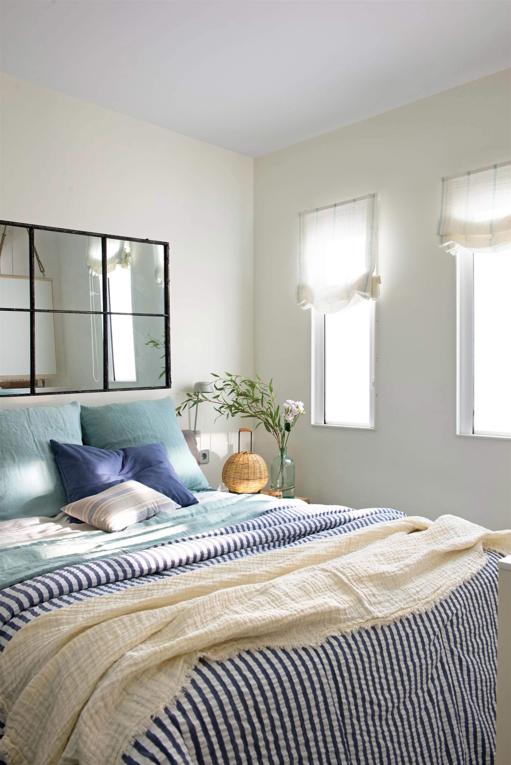 Dormitorio con ropa de cama a rayas azules y espejo de cuarterones sobre el cabecero.
