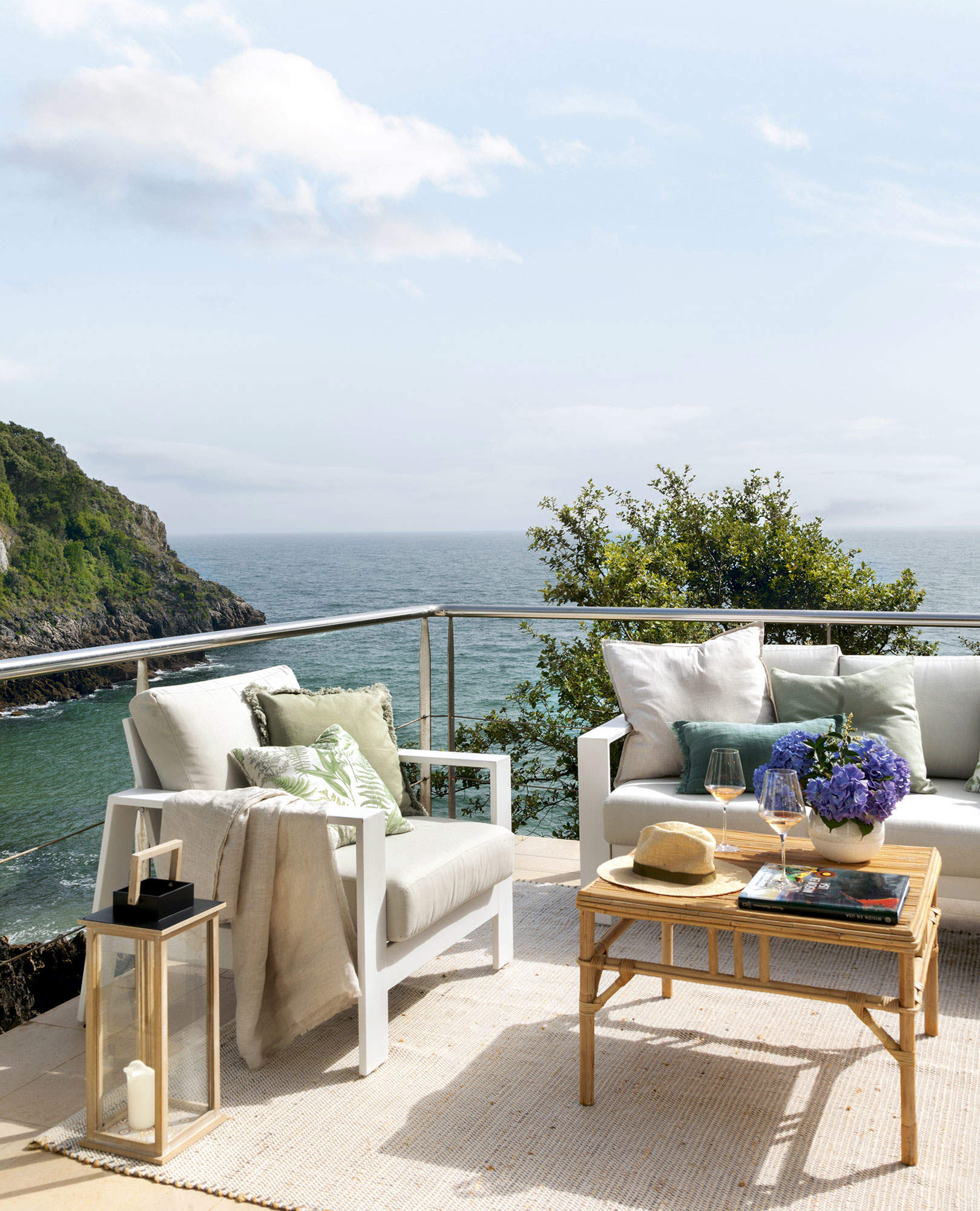 Balcón con vistas al mar con sofá y butaca de metal blanco y mesa de fibras 561739