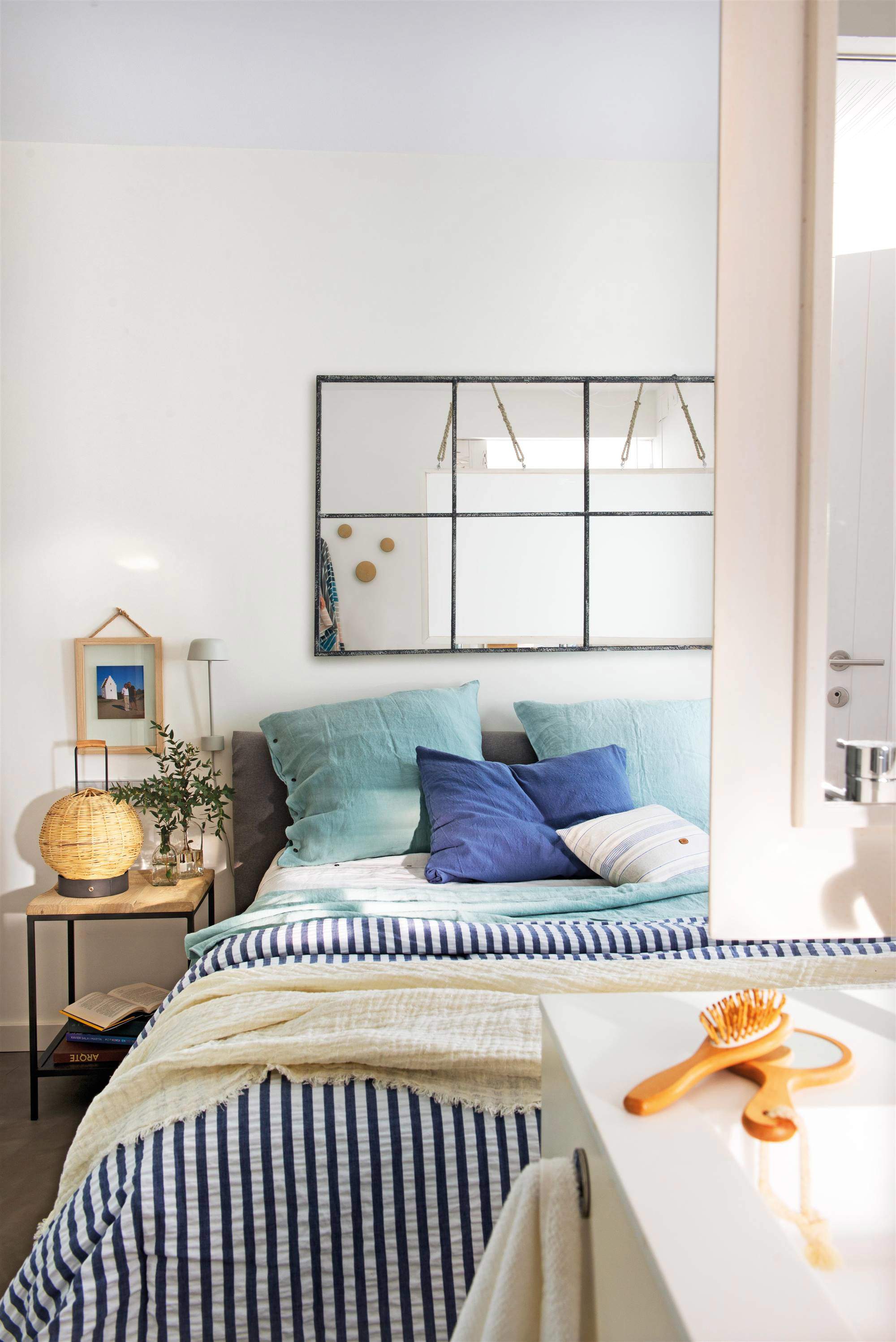Dormitorio decorado en blanco y azul con espejo en la pared de la cama