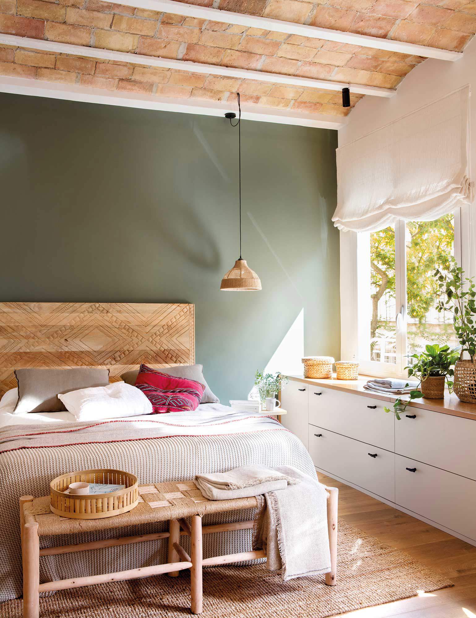 Dormitorio con pared verde, mueble bajo la ventana y cabecero de madera.