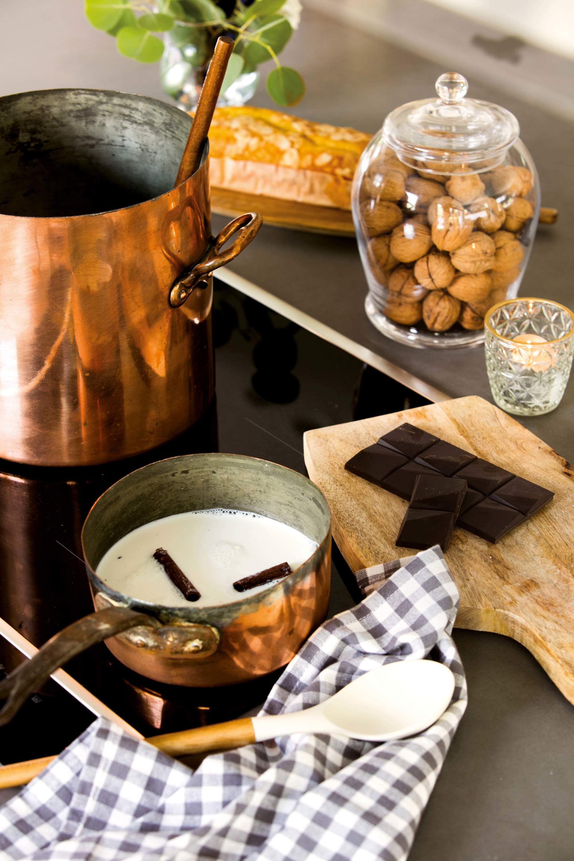 Menaje de cobre, onza de chocolate y nueces sobre encimera de cocina oscura.