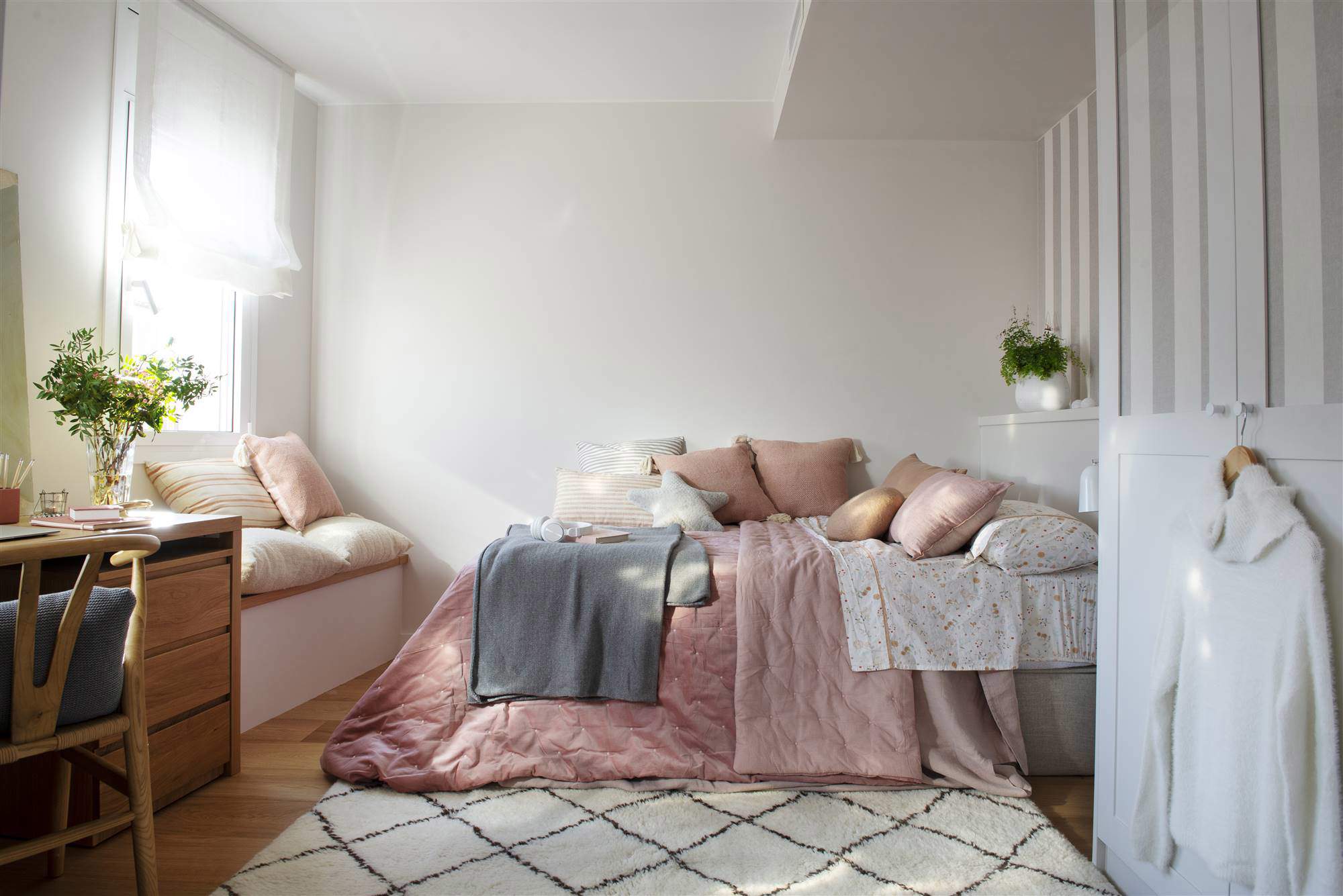 Dormitorio juvenil con ropa de cama rosa y banco bajo la ventana.