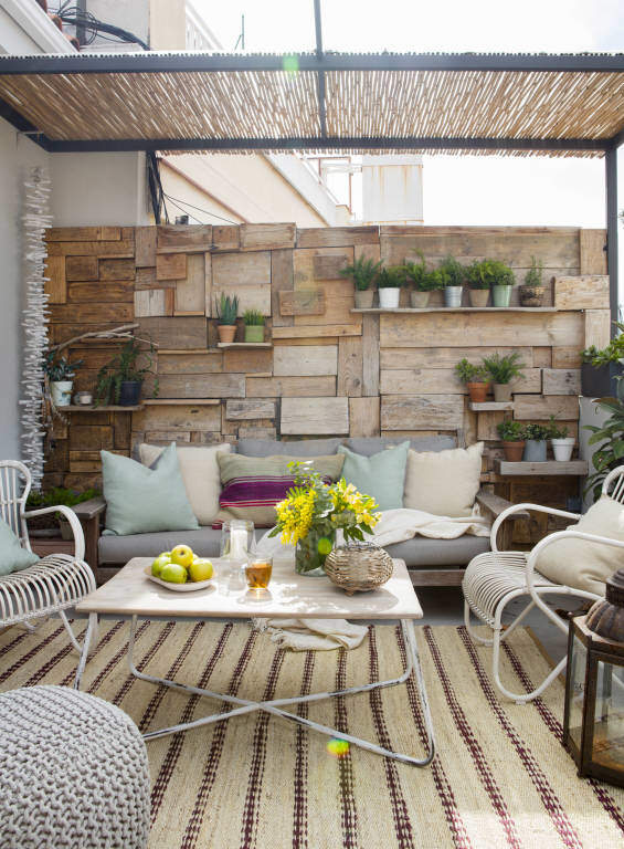 Terraza pequeña con pérgola de cañizo y pared de madera para colocar plantas en baldas.