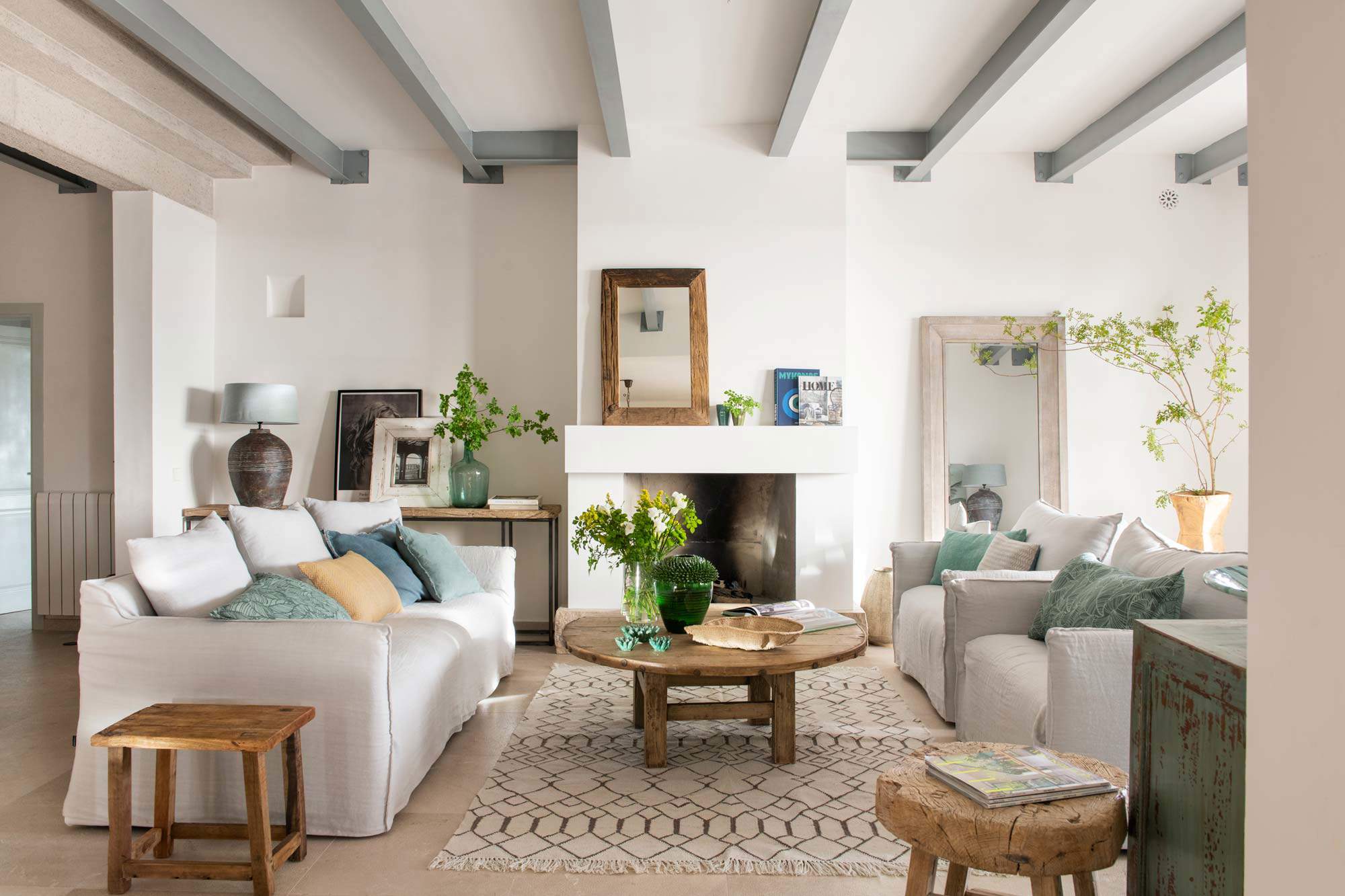 Salón con vigas en el techo lacadas en gris, chimenea, sofás enfrentados y mesa redonda de madera.
