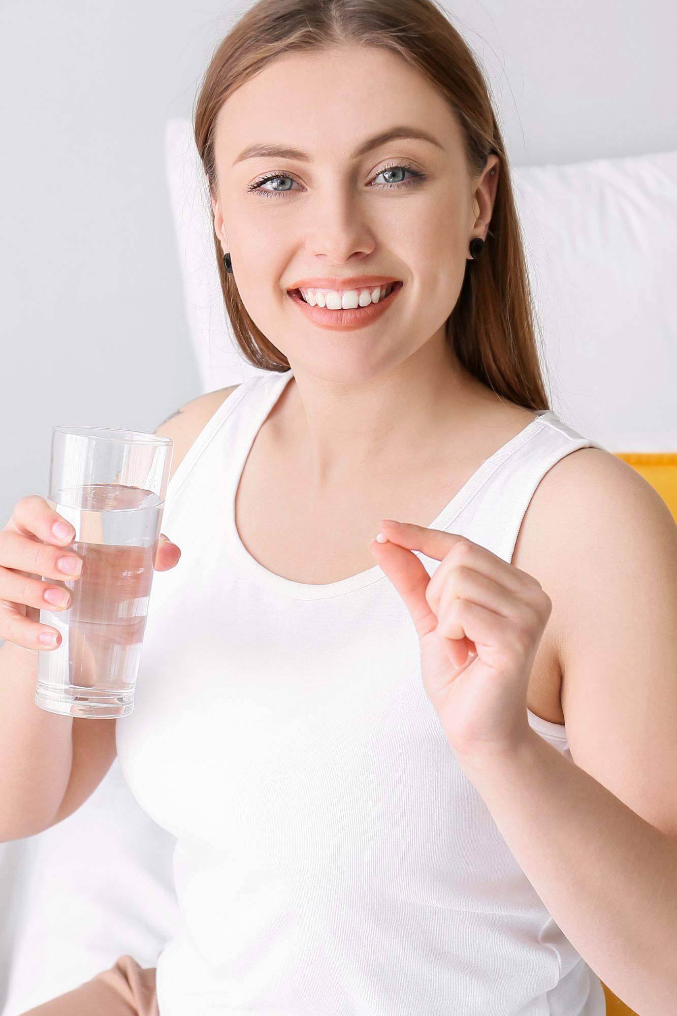 Chica tomando una pastilla con un vaso de agua.
