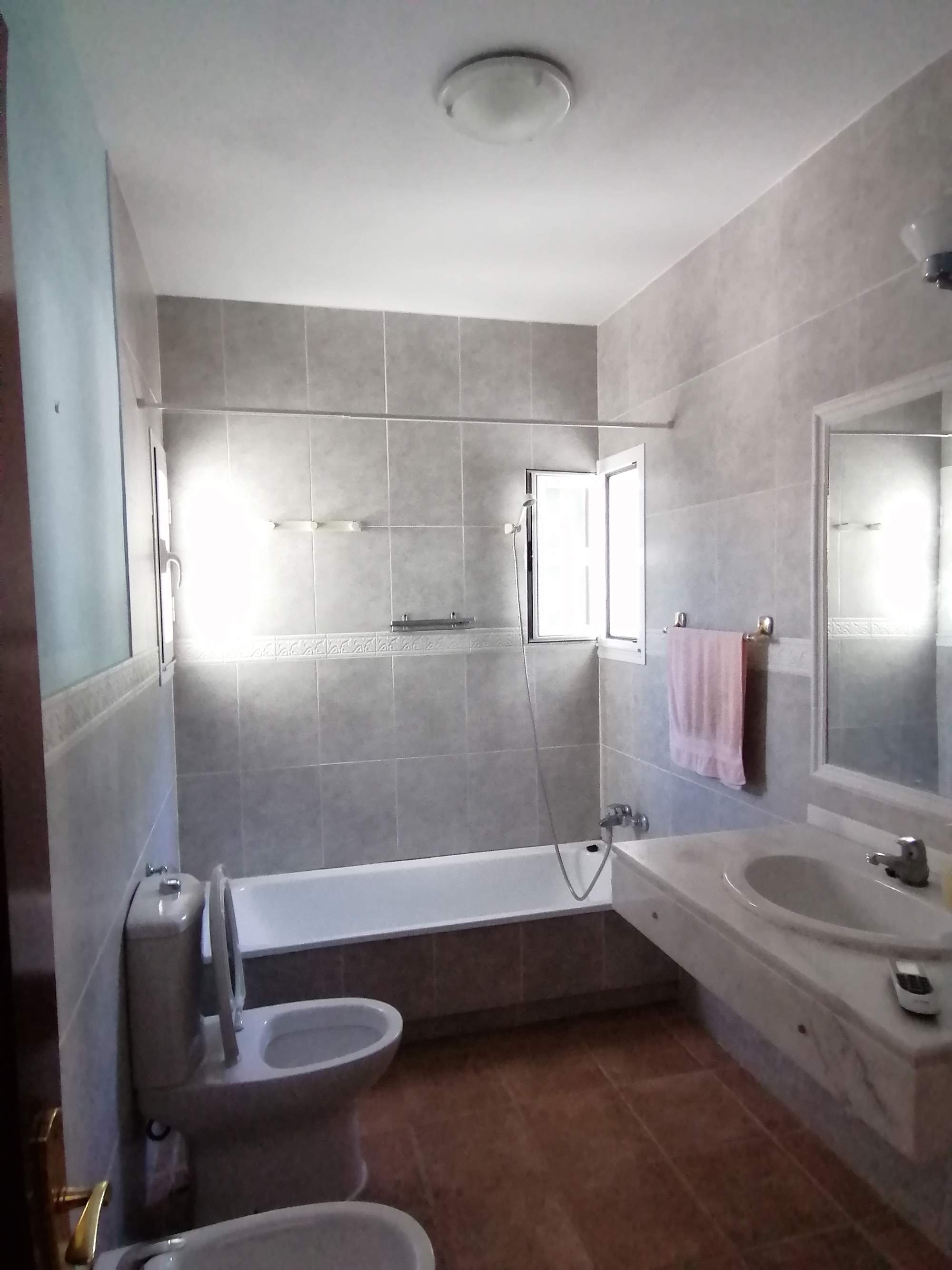 Un baño principal con baldosas en suelo y paredes, lavabo de mármol y apariencia anticuada.