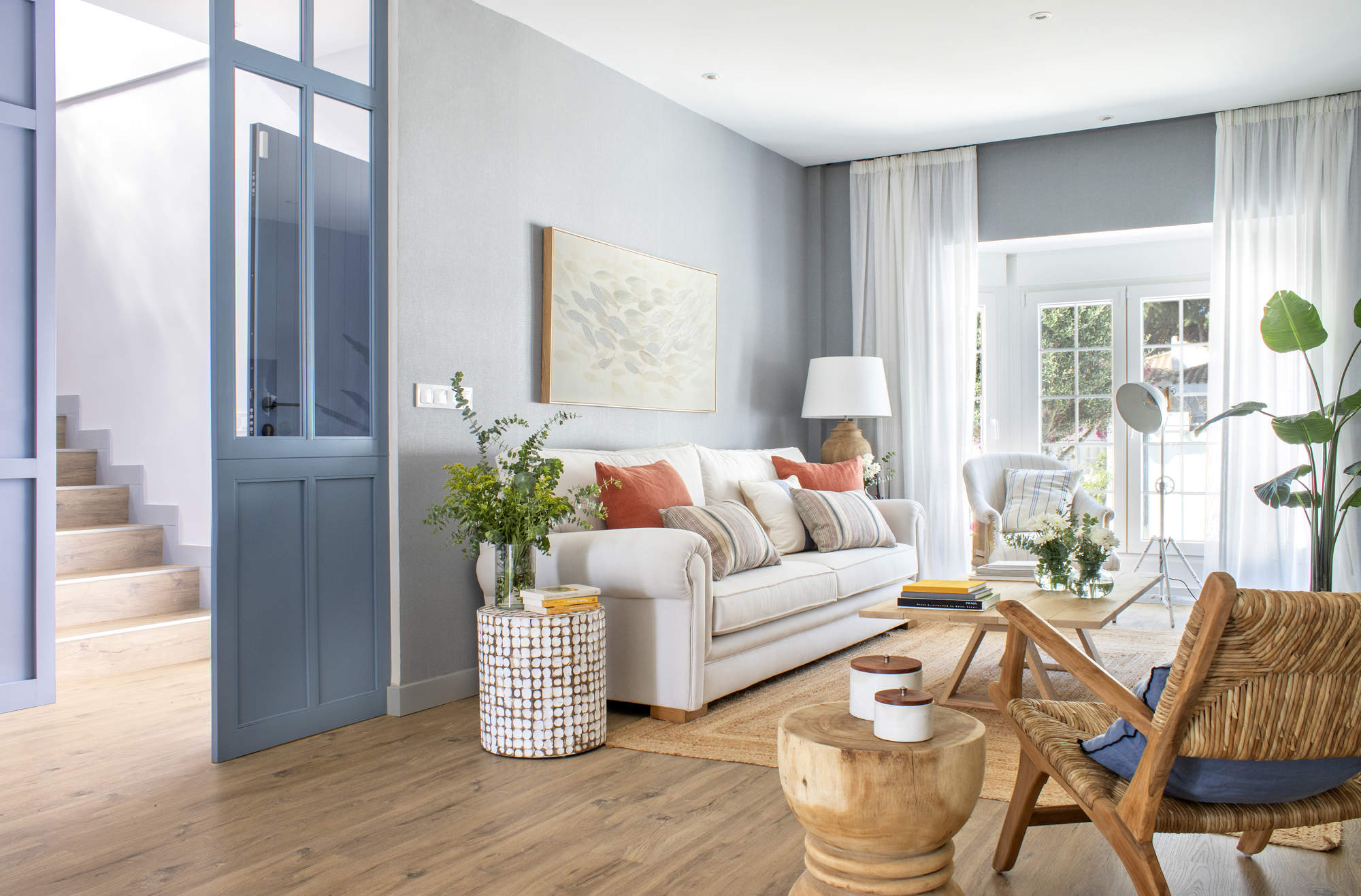 Un salón luminoso en tonos azules y blancos, con predominio de madera y detalles naturales con plantas.