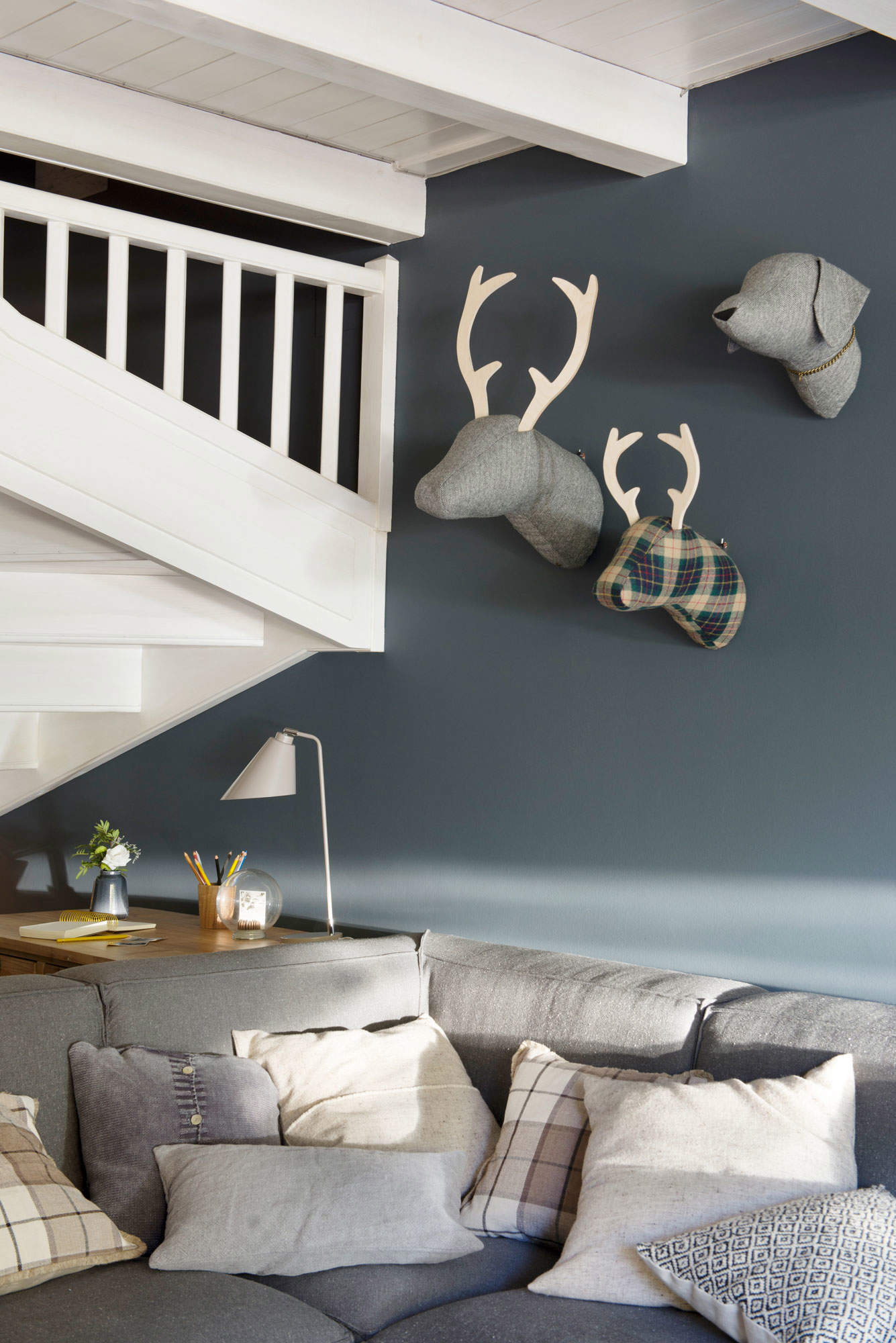Salón con sofá gris, cojines de cuadros y pared azul.