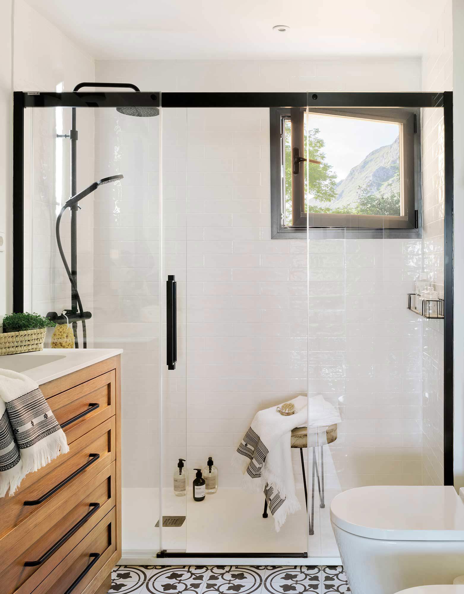 Un baño con una gran ducha con mampara con estructura negra.