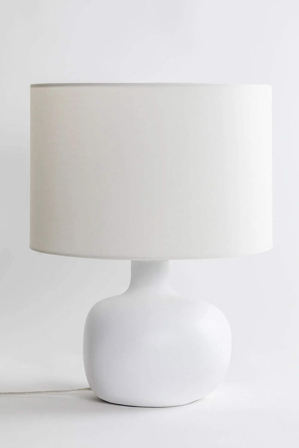 Lámpara de mesa con base en forma de botella y pantalla blanca.