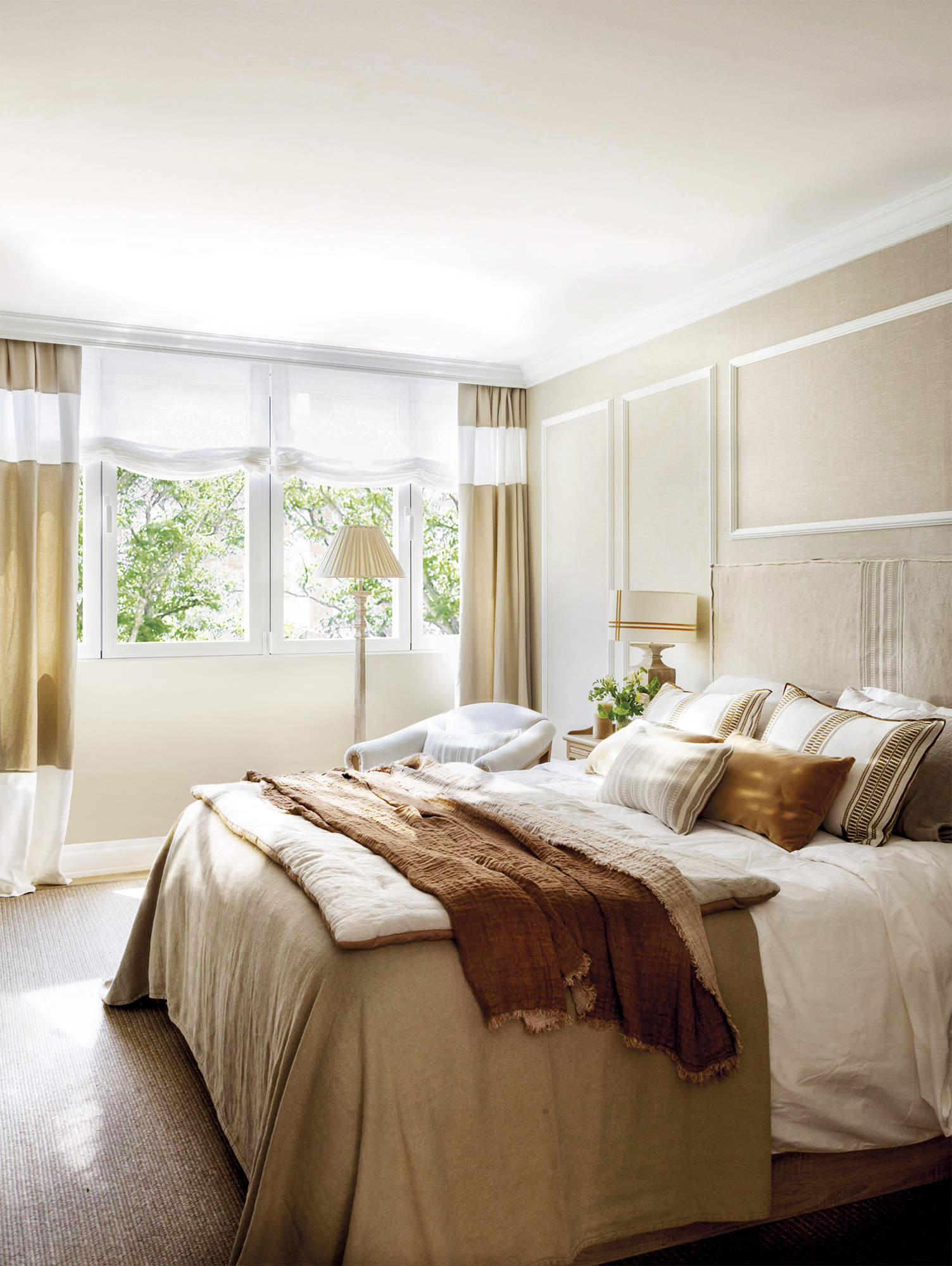 Dormitorio principal con pared con molduras, cabecero, ropa de cama de colores tierra.