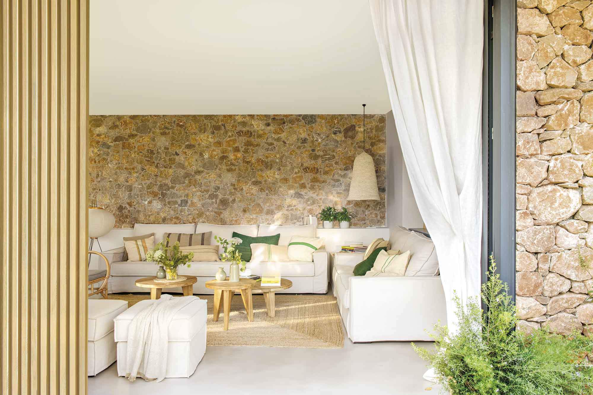 Salón con sofás blancos, pared de piedra desnuda y alfombra de fibras.
