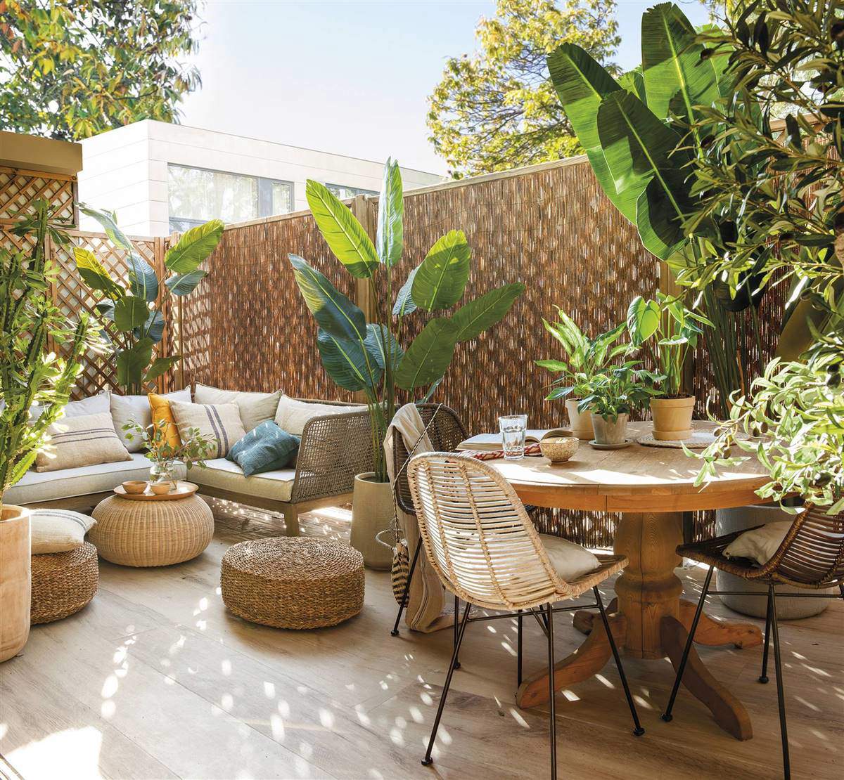 Terraza interior con plantas de exterior, sofá, comedor exterior y muebles de fibras. 