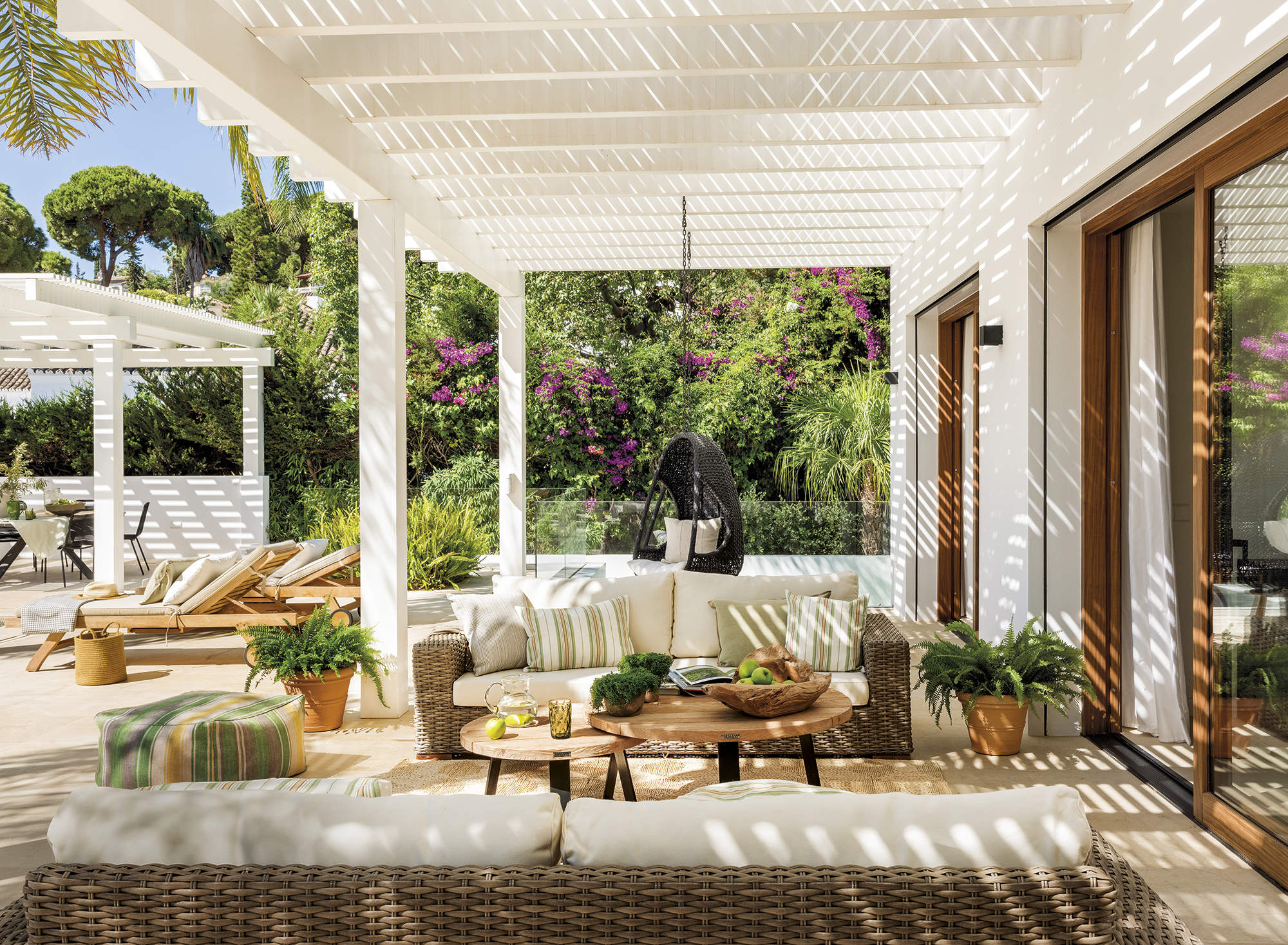 Porche con pérgola blanca y sofás de mimbre. 