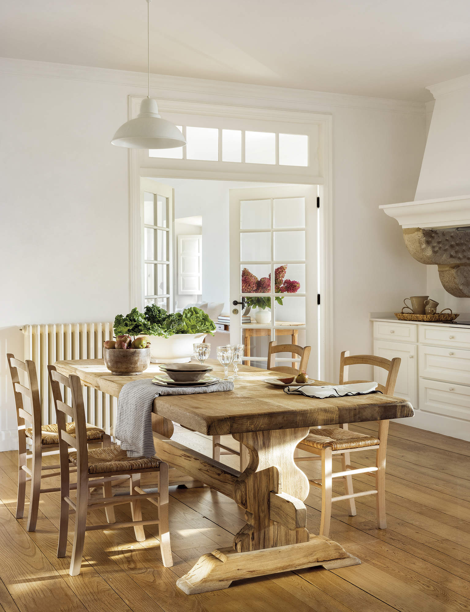 cocina con comedor, mesa de madera rústica con sillas de madera, lámpara de techo blanca, suelo de madera natural