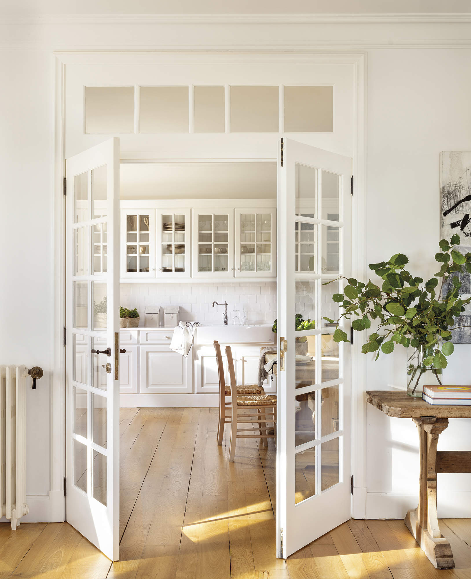 cocina con puertas acrisoladas blancas, suelo de madera natural con muebles blancos, mesa y sillas de madera, planta