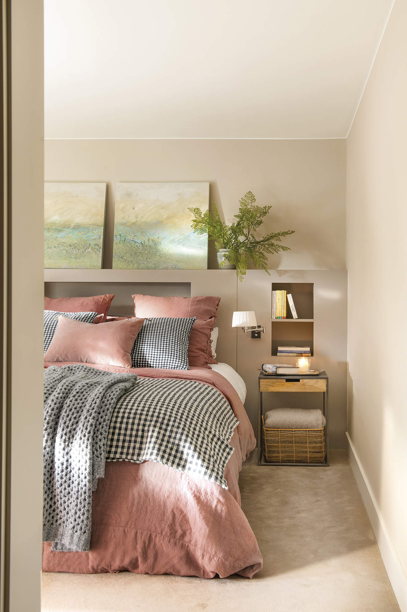 Dormitorio principal con moqueta beige, cama con cabecero de obra, cuadros, ropa de cama rosada y gris a cuadros.