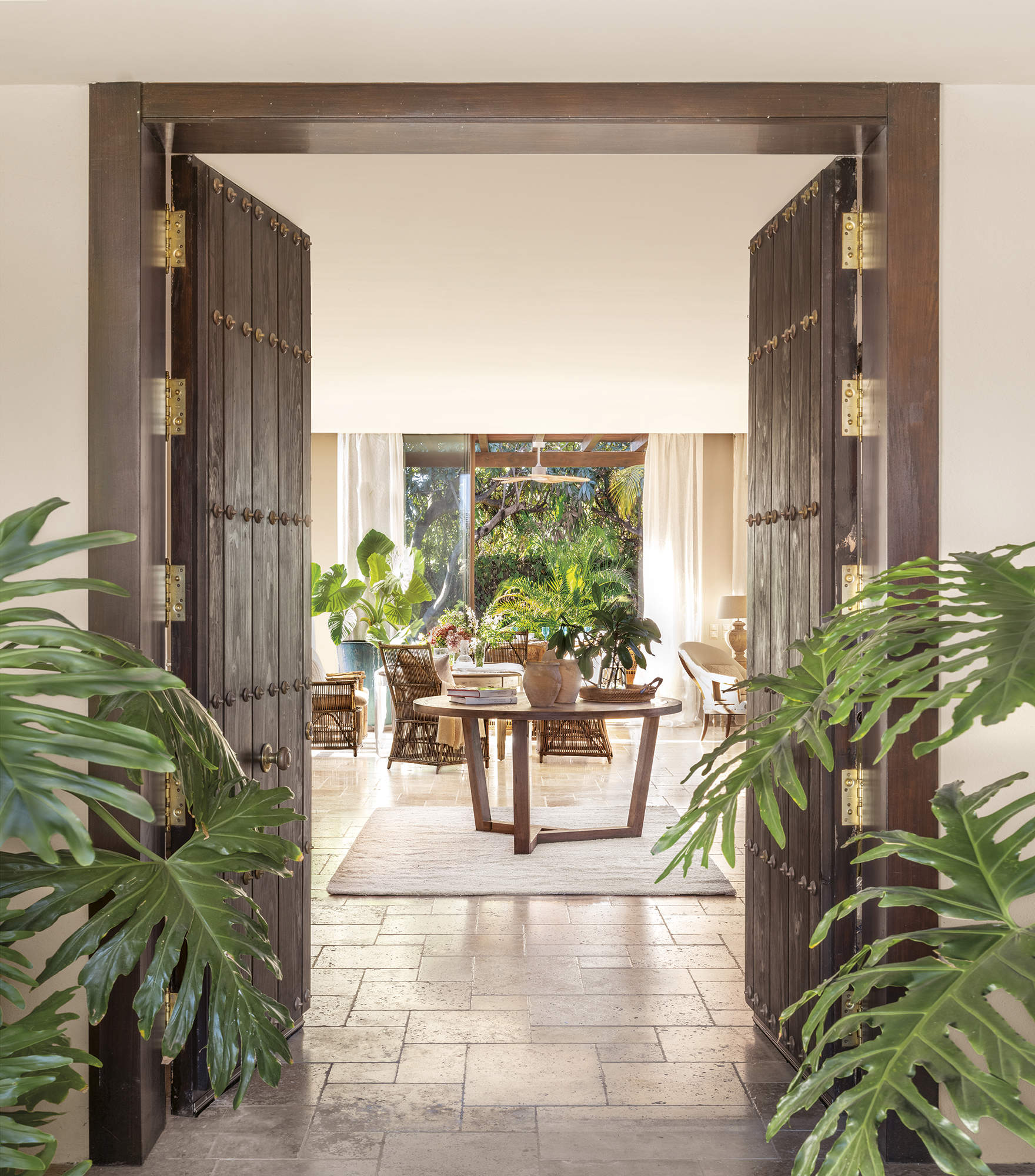 recibidor con puertas de madera con herrajes, pavimento de piedra natural, plantas, alfombra y mesa de madera redonda, porche al fondo