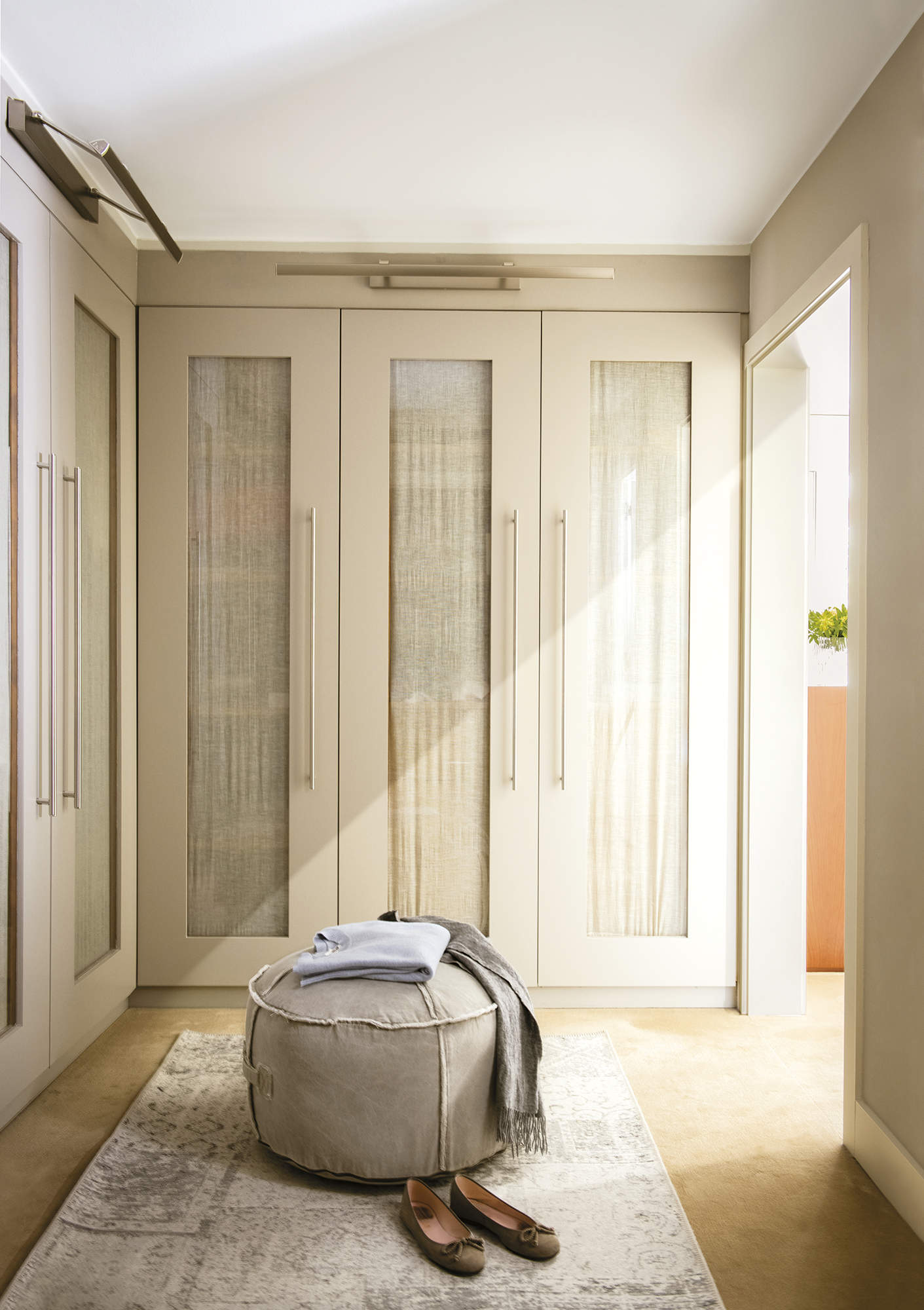 Vestidor con armarios empotrados con puerta con cristal, iluminados, puf, moqueta y alfombra.