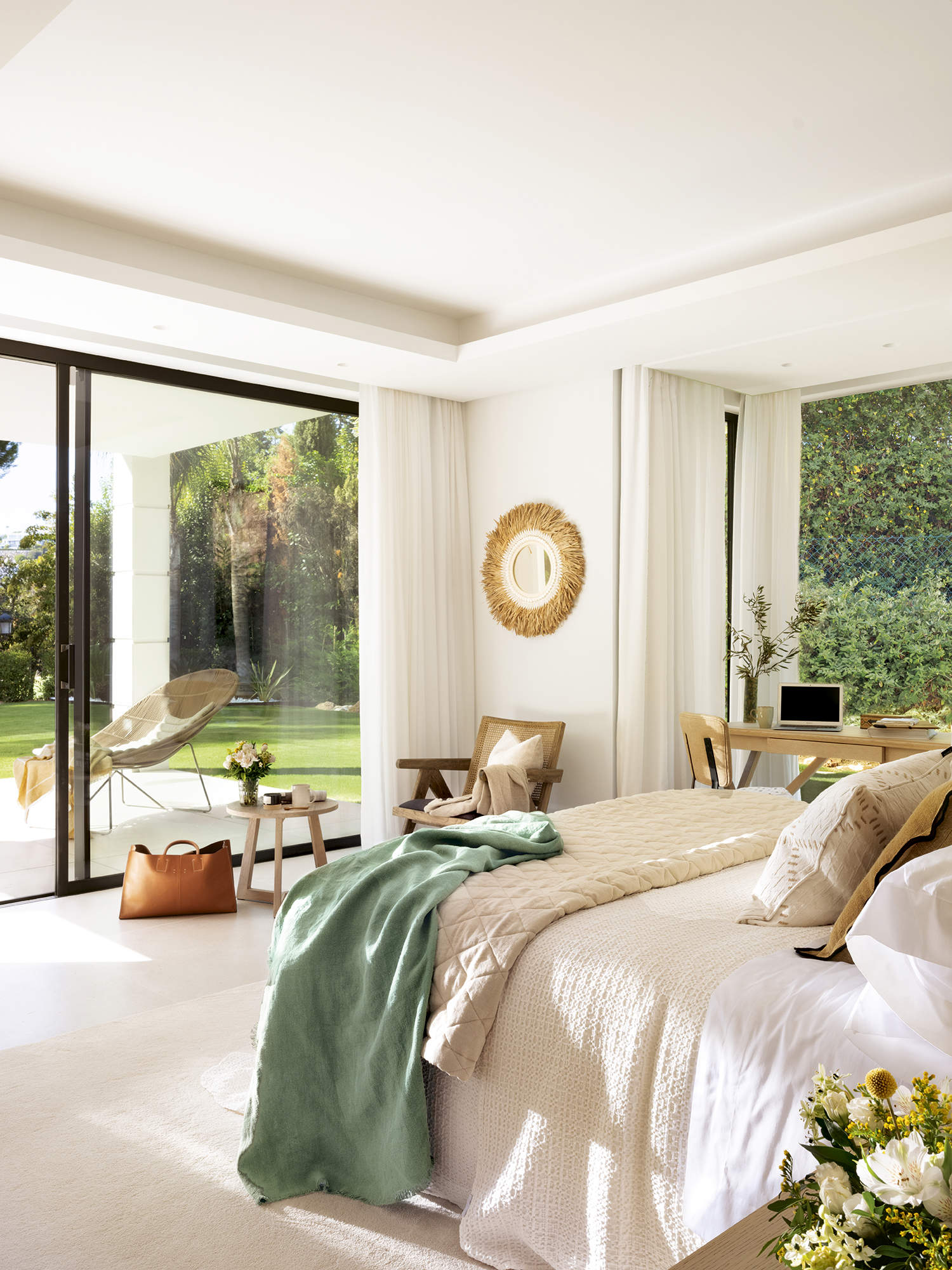 Dormitorio principal con ropa de cama beige con plaid verde, escritorio de madera, butaca y mesa auxiliar