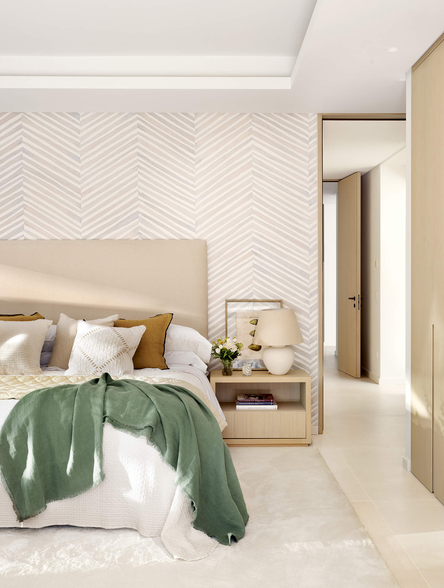 Dormitorio principal, pared empapelada, cabecero tapizado, mesa de noche con lámpara, alfombra blanca