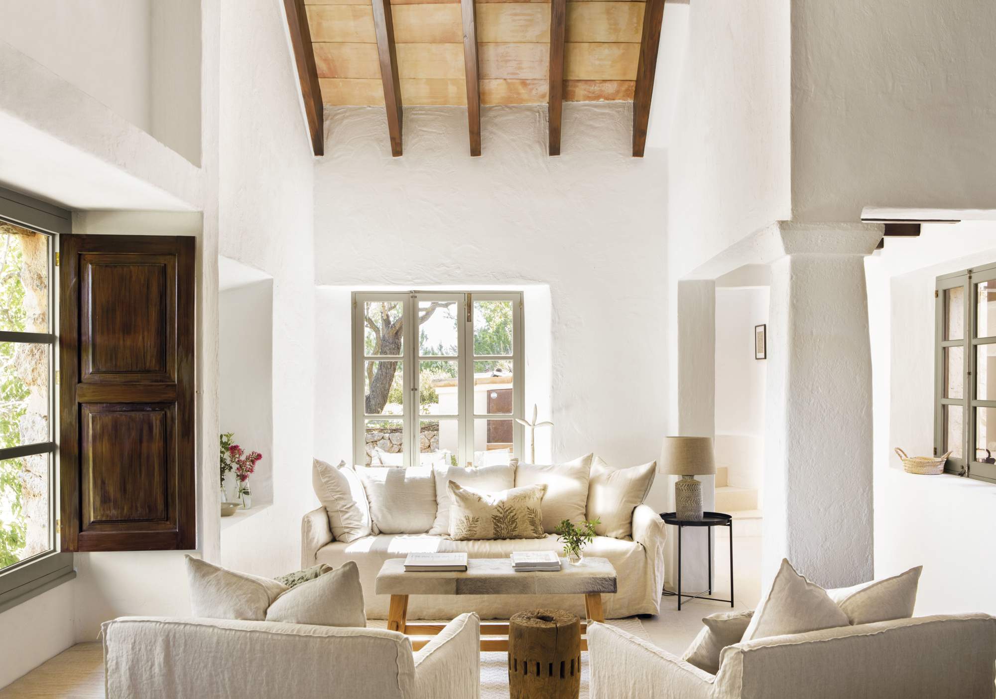 Salón con sofá de color blanco, dos butacas y ventana de madera.