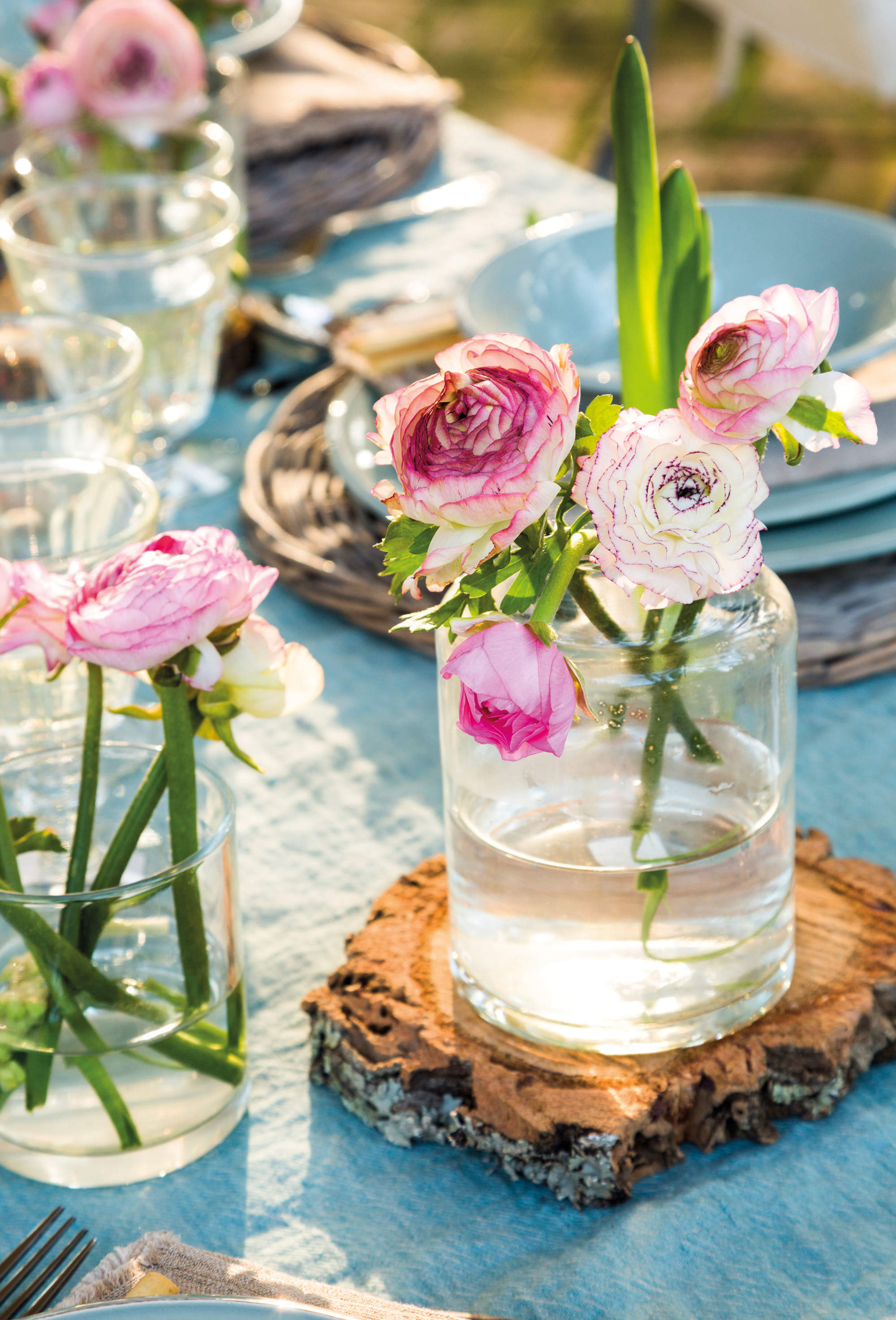 Detalle de mesa con mantel y vajilla azules y jarrones con flores.