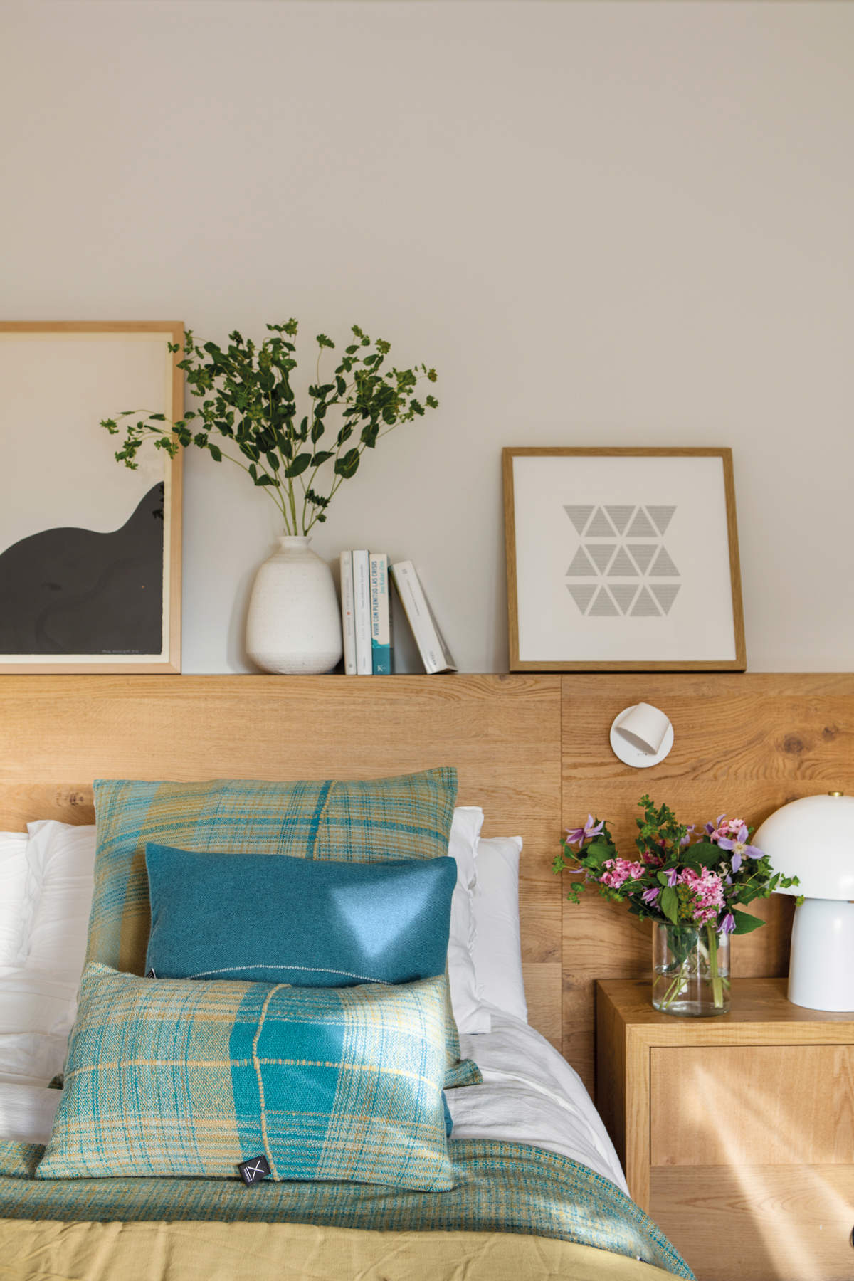 Dormitorio con cabecero en madera, flores frescas y cuadros.