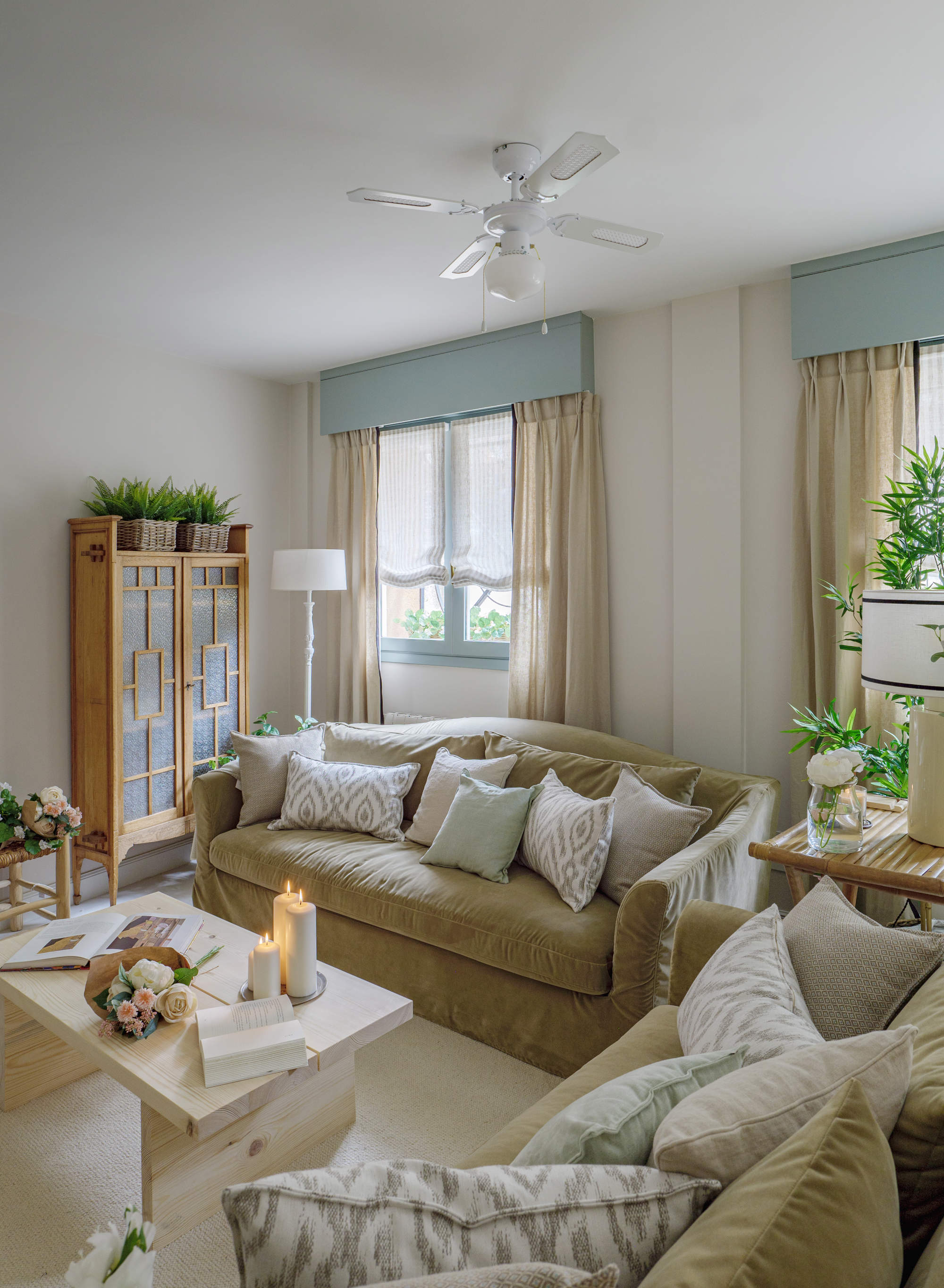 Salón con sofás verdes, ventanas azules y alacena de madera de anticuario.