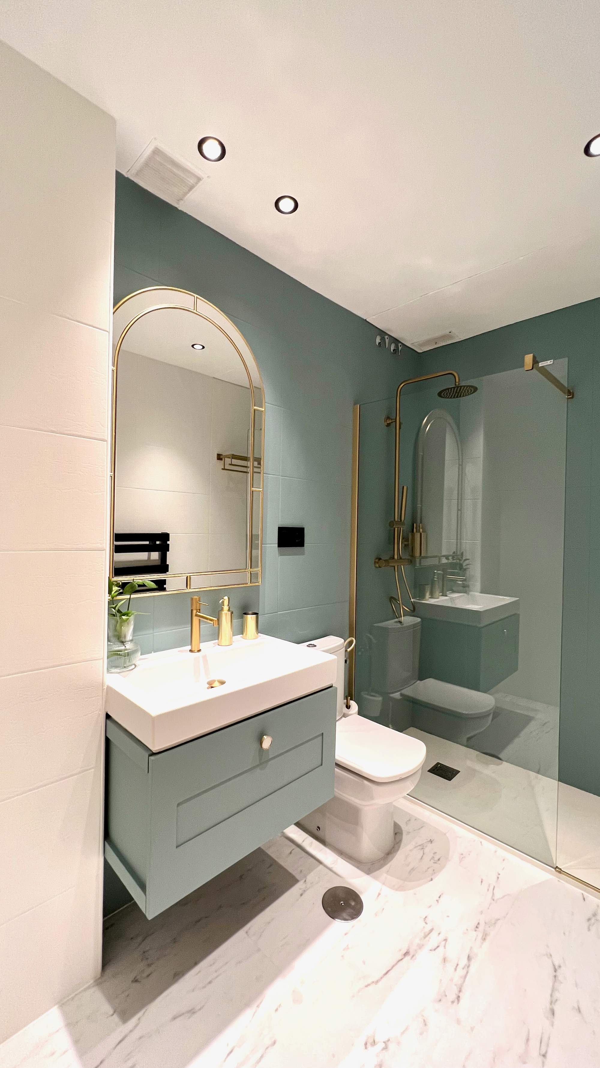 Baño con mueble de color verde azulado, igual que la pared, y ducha con perfil dorado. 