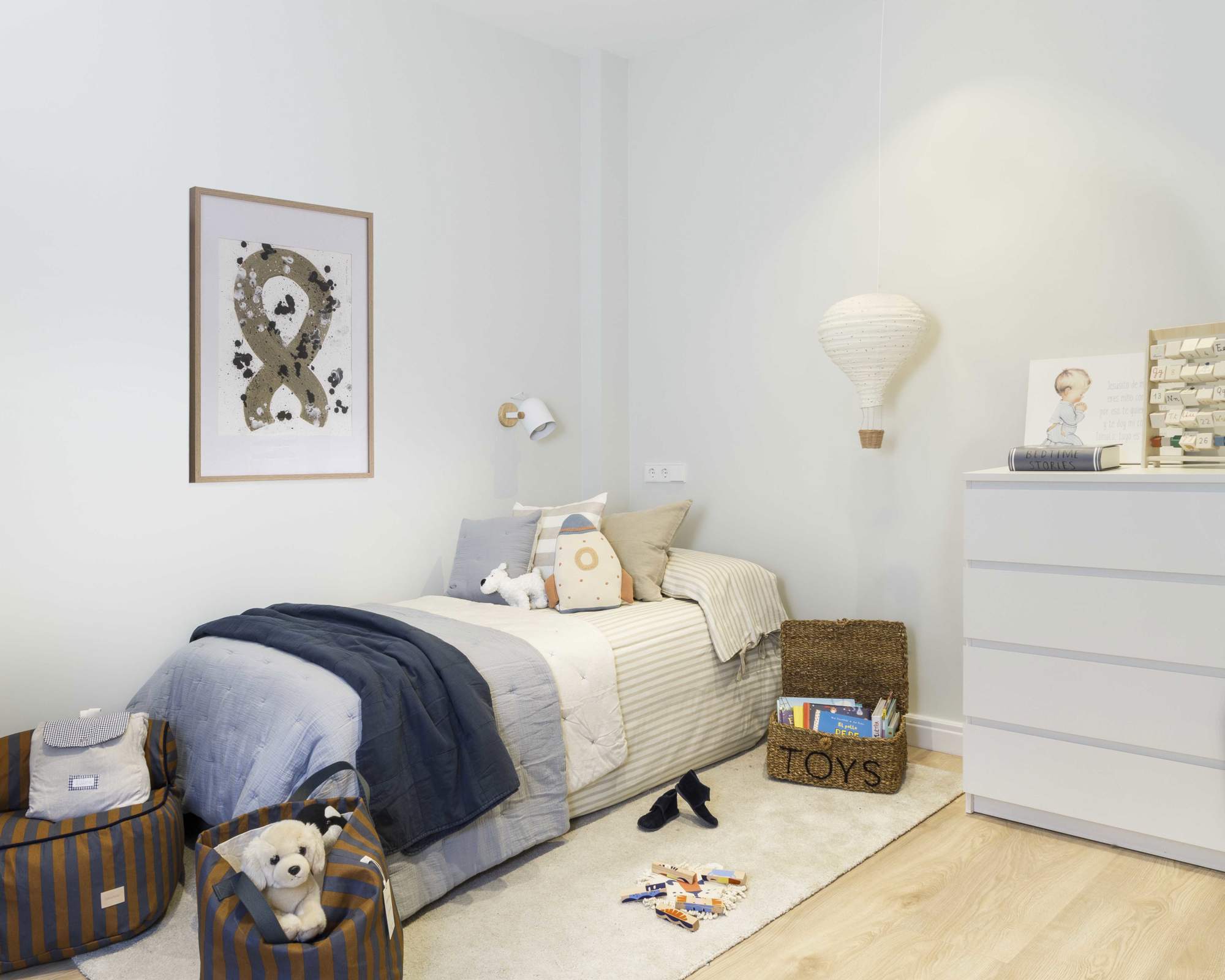 Dormitorio infantil decorado con puff y cesto a rayas de Nobodinoz, colchas de Zara Home, y cesta de mimbre de H&M Home.