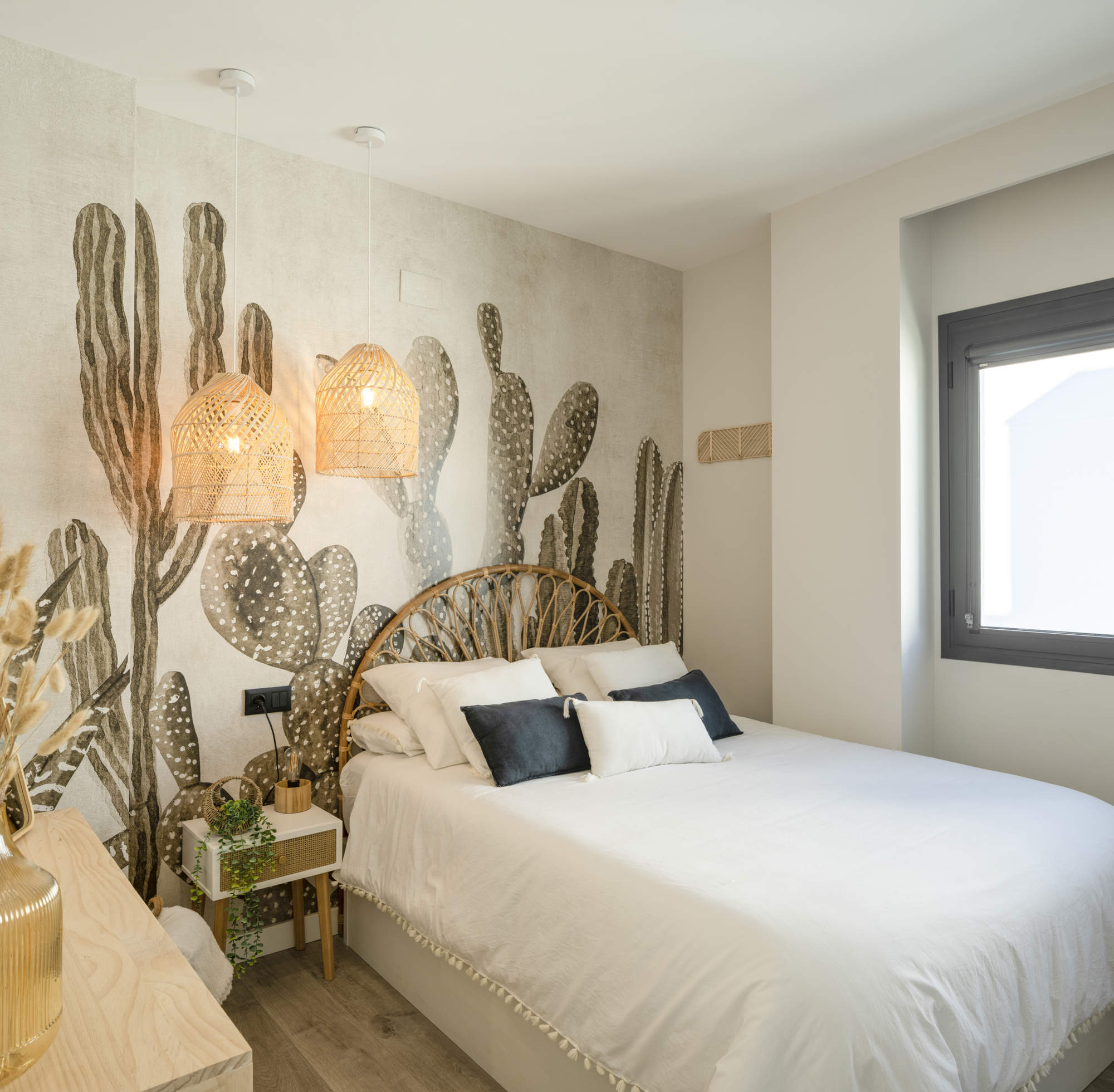 Dormitorio juvenil con cabecero y lámparas rústicas, colcha con borlas de flecos, decoración de plantas en la mesilla y en el papel pintado de cactus.