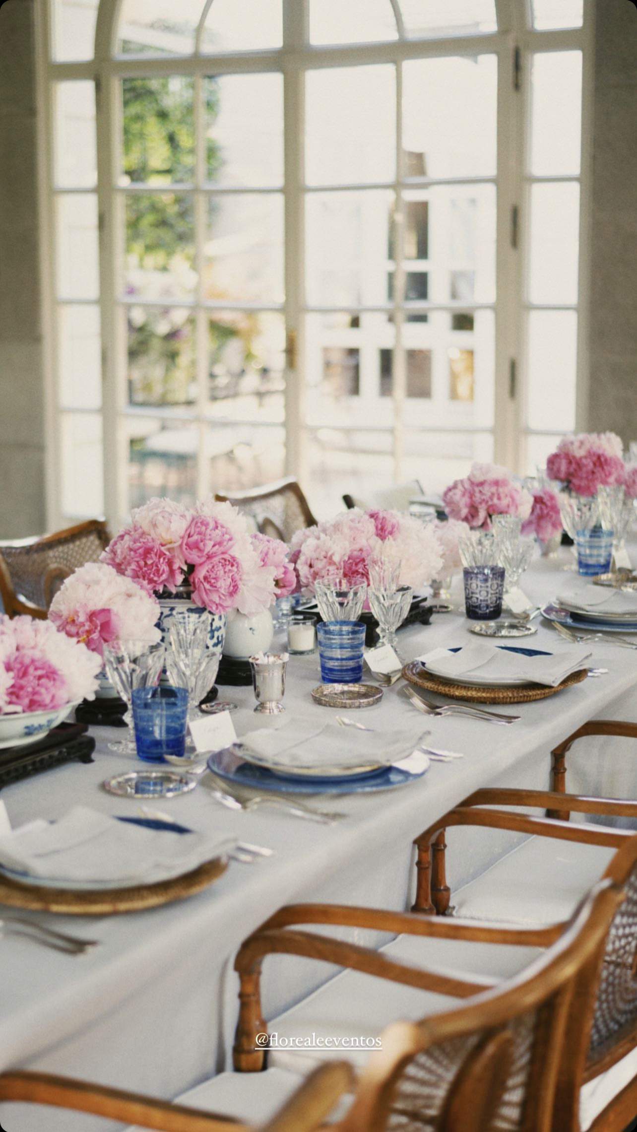Una mesa con manteles blancos, vajilla con detalles en azul y flores rosas