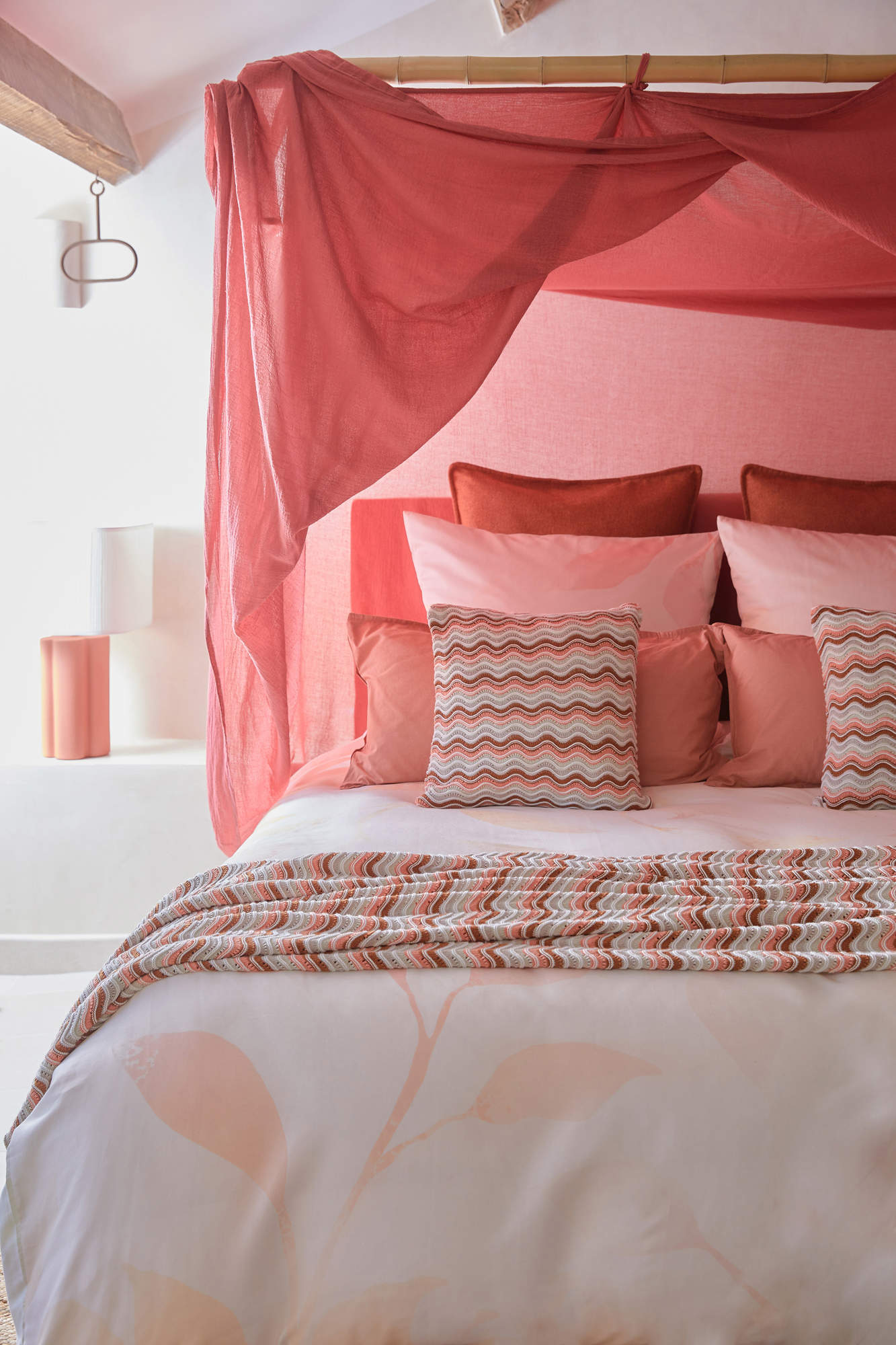 Dormitorio con dosel y textiles en tonos rosas.