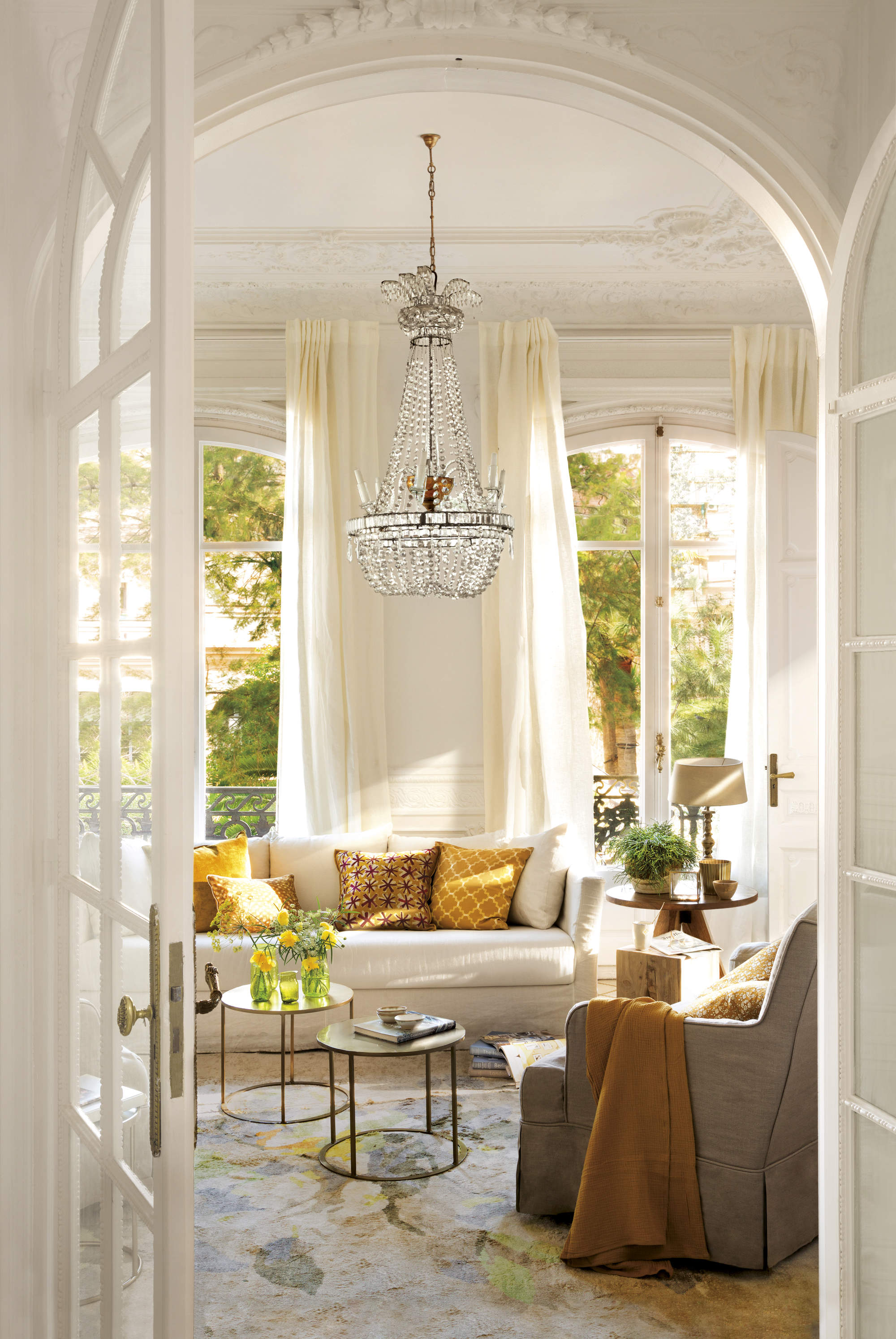 Salón decorado con sofá beige, cojines amarillos, tierra y. mostazas y lámpara de araña. 