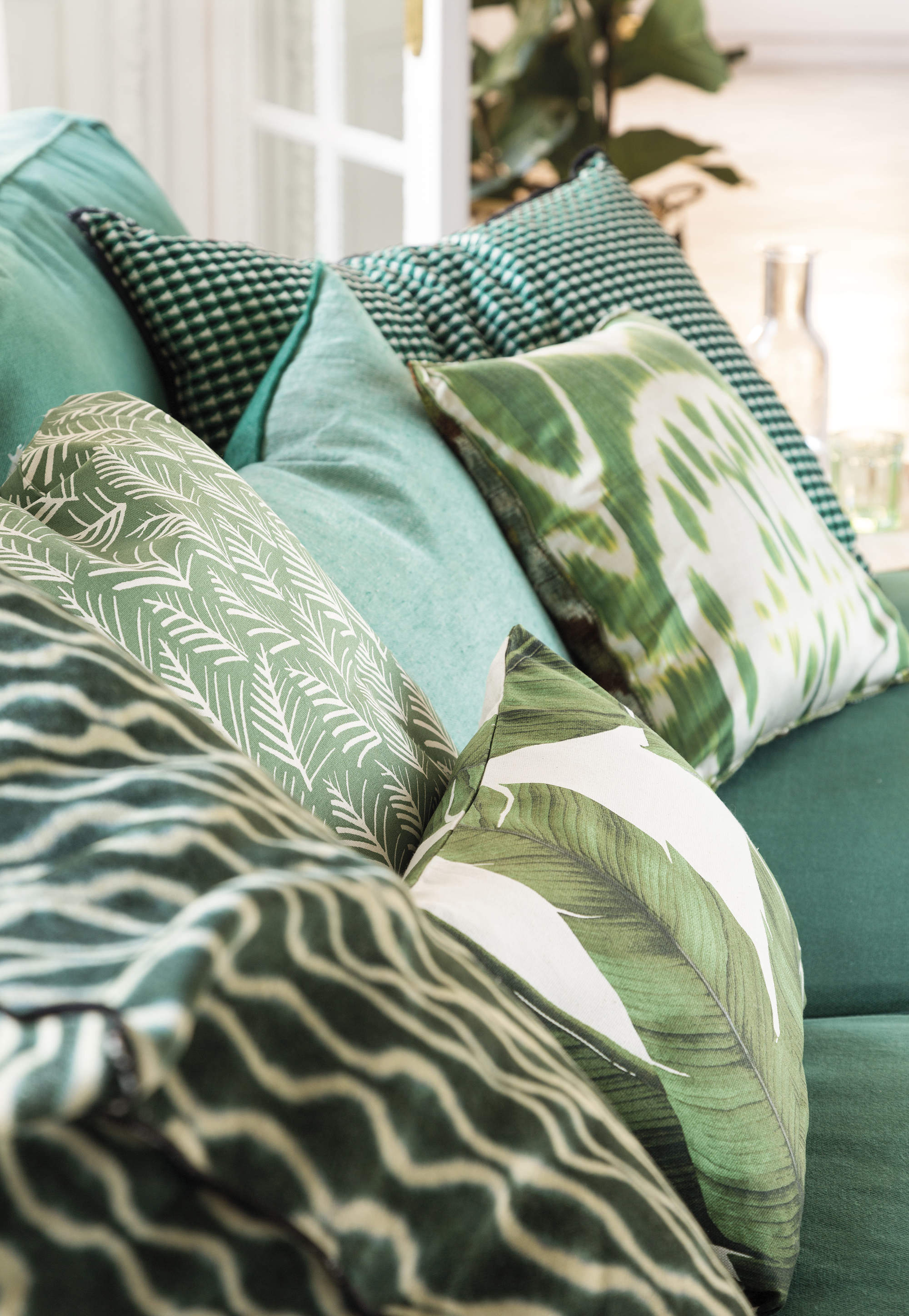 Salón con sofá verde decorado con cojines a rayas y botánicos de color verde. 