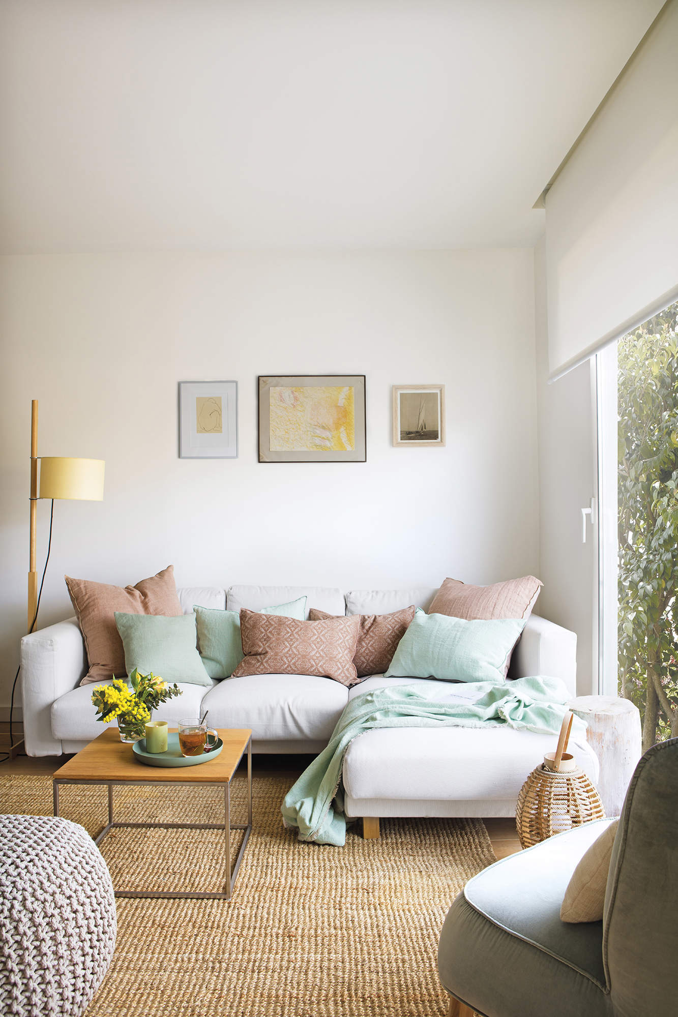 Salón con sofá blanco, alfombra de fibra y cojines en tonos verdes y rosas.
