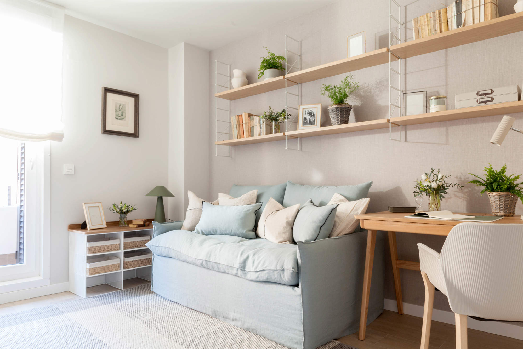 Estancia decorada con un sofá-cama en tonos azules, y mobiliario minimalista con acabados de madera.
