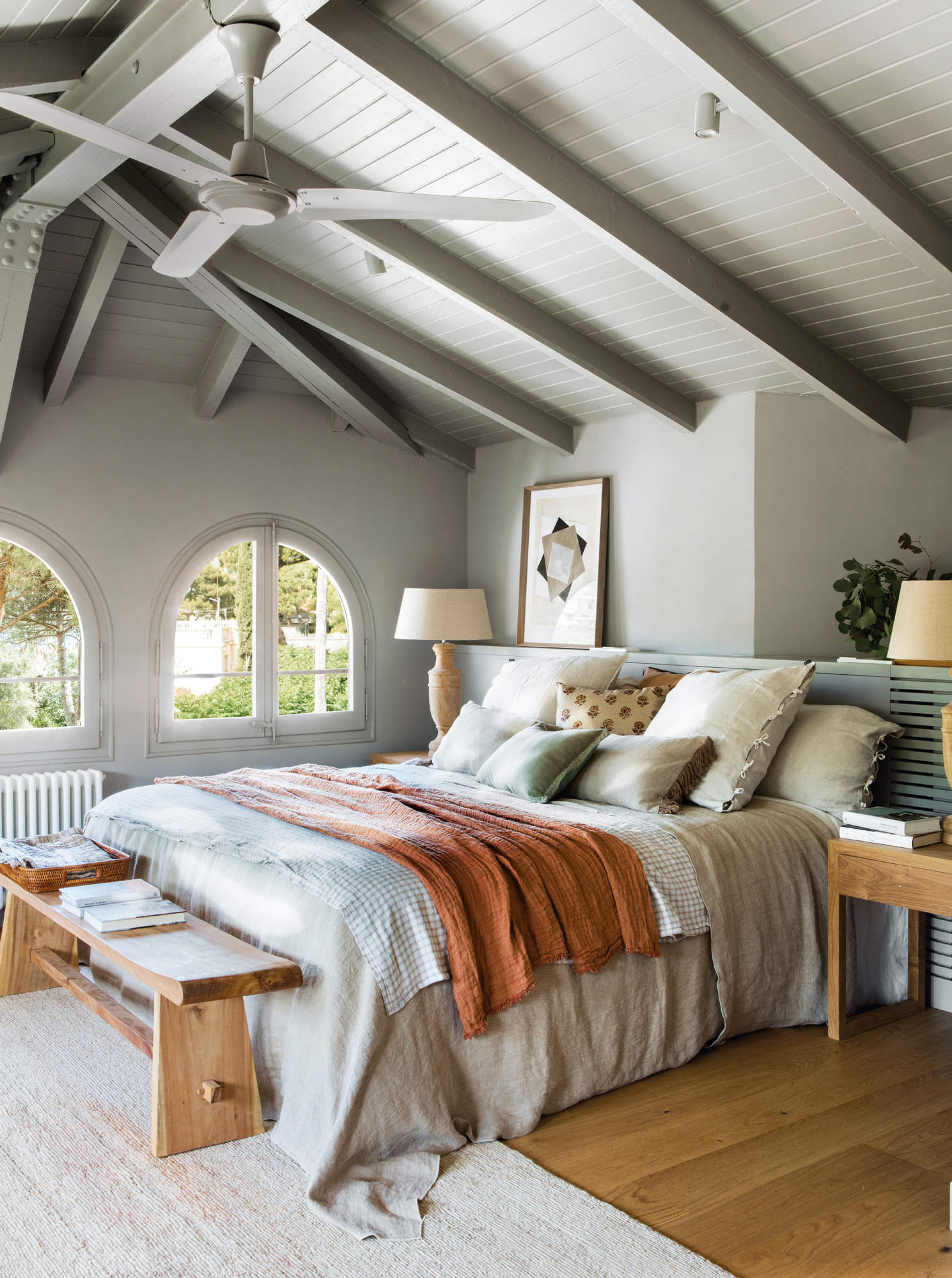 Dormitorio decorado en tonos grises, con ropa de cama en tonos tierra, y vigas a la vista.