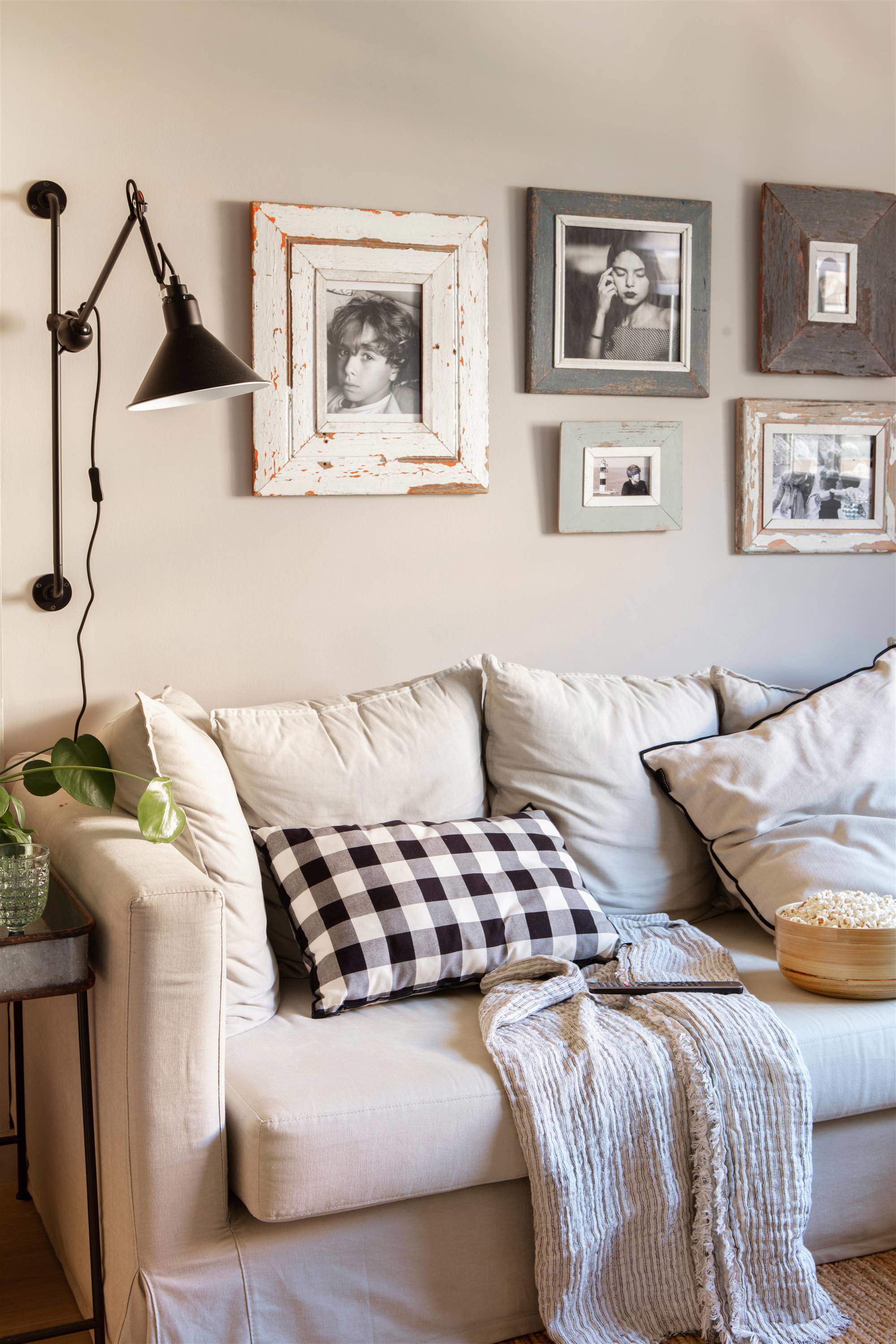 Salón con sofá, cojín de cuadros y pared decorada con fotografías en blanco y negro.