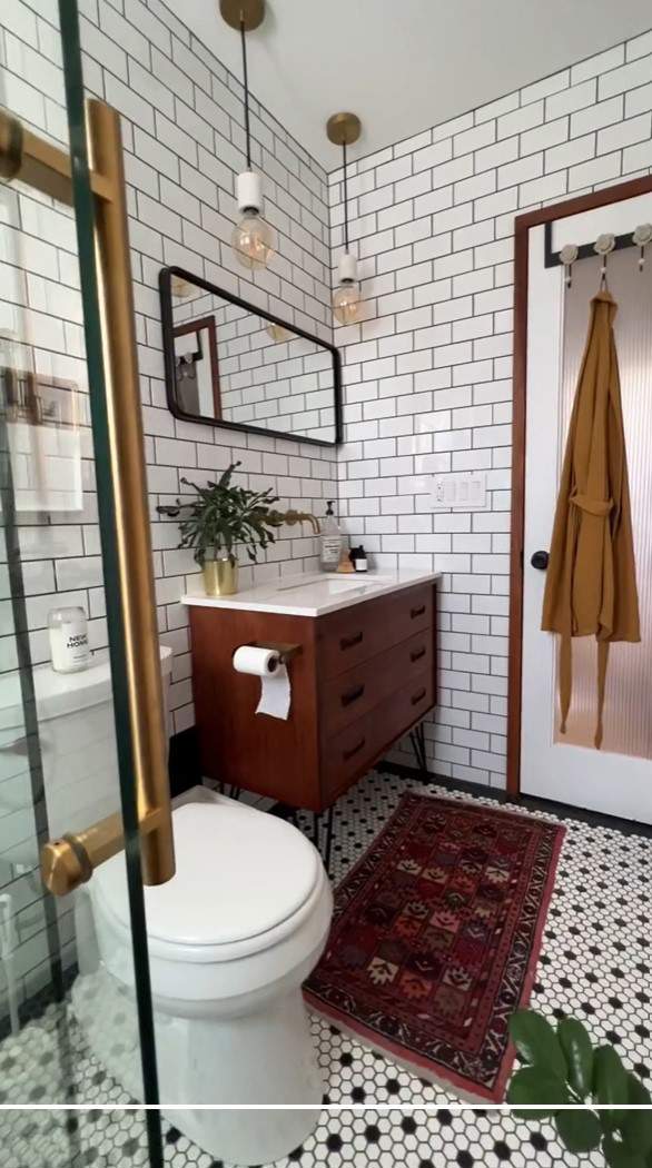 Baño con azulejos y baldosas blancas y negras, mueble bajolavabo de madera y alombra.