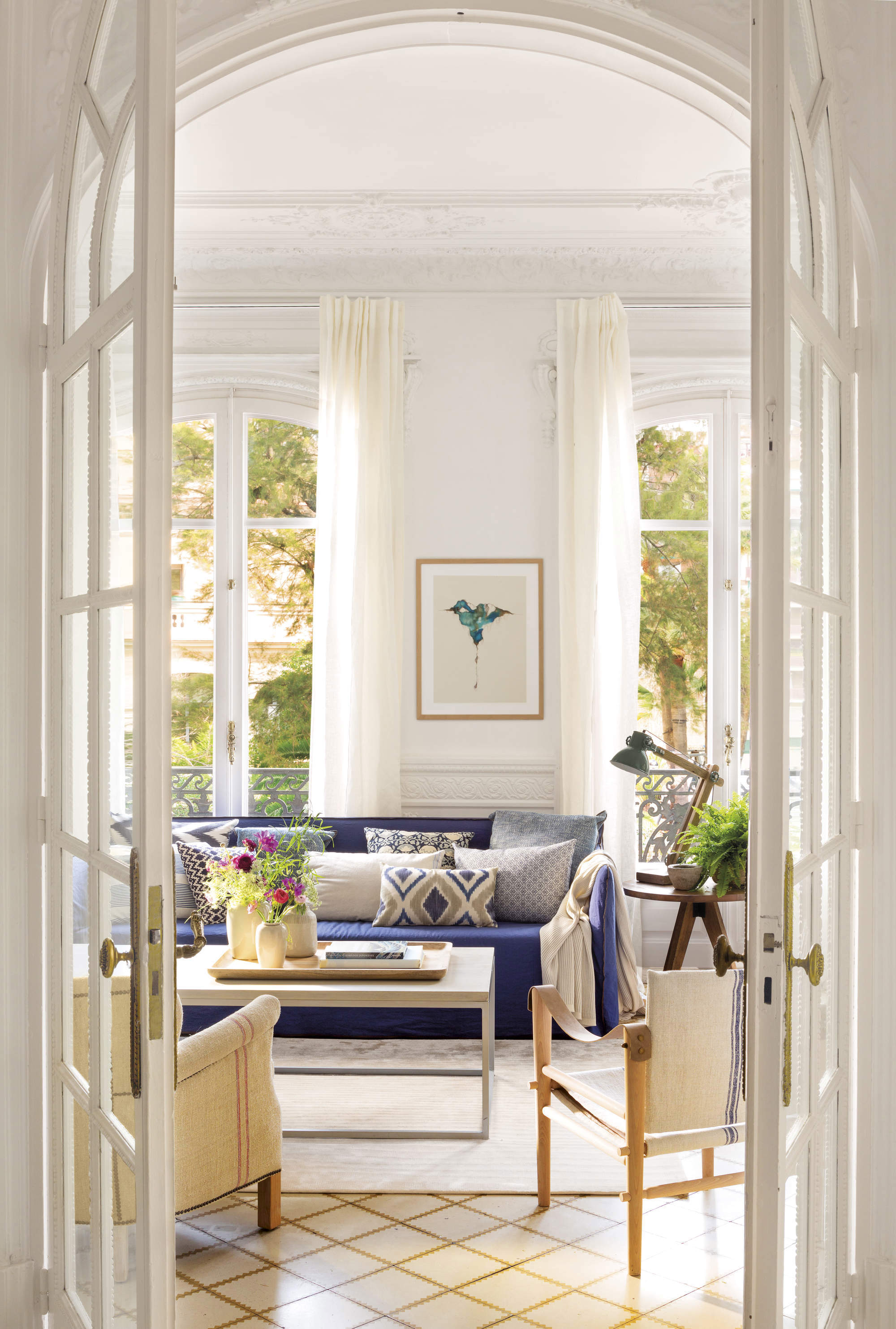 Salón con sofá azul, maxi alfombra blanca y butacas acabadas en madera.