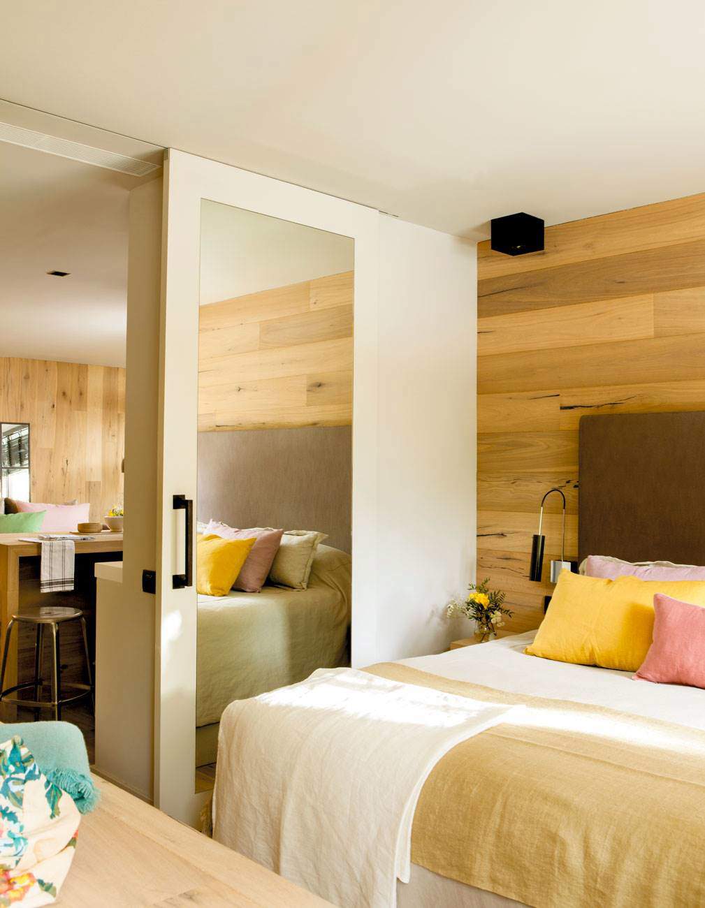 Dormitorio con puerta corredera y espejo y pared del cabecero de madera.