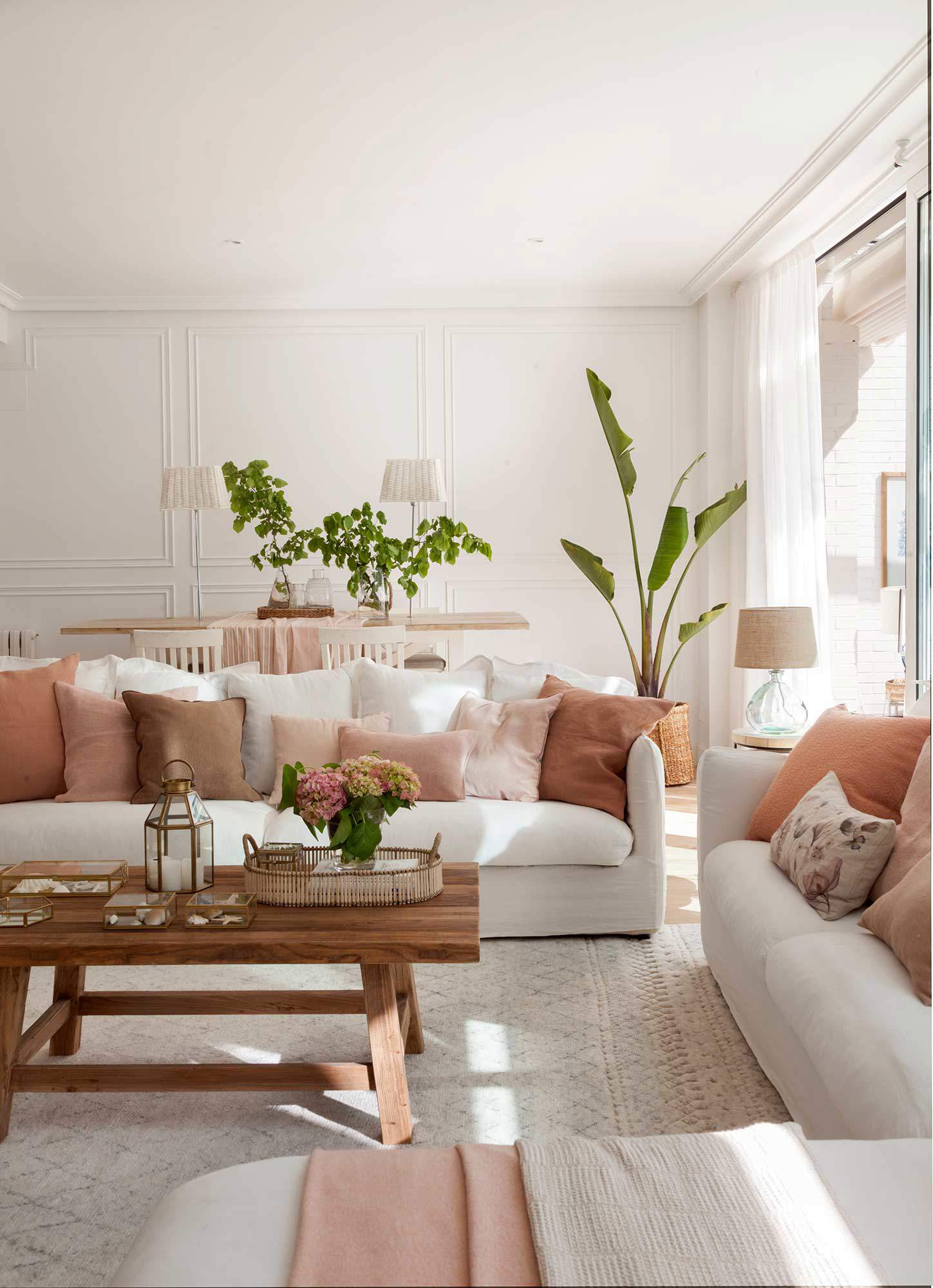 Salón con sofás blancos y cojines en tonos tierra y rosados.