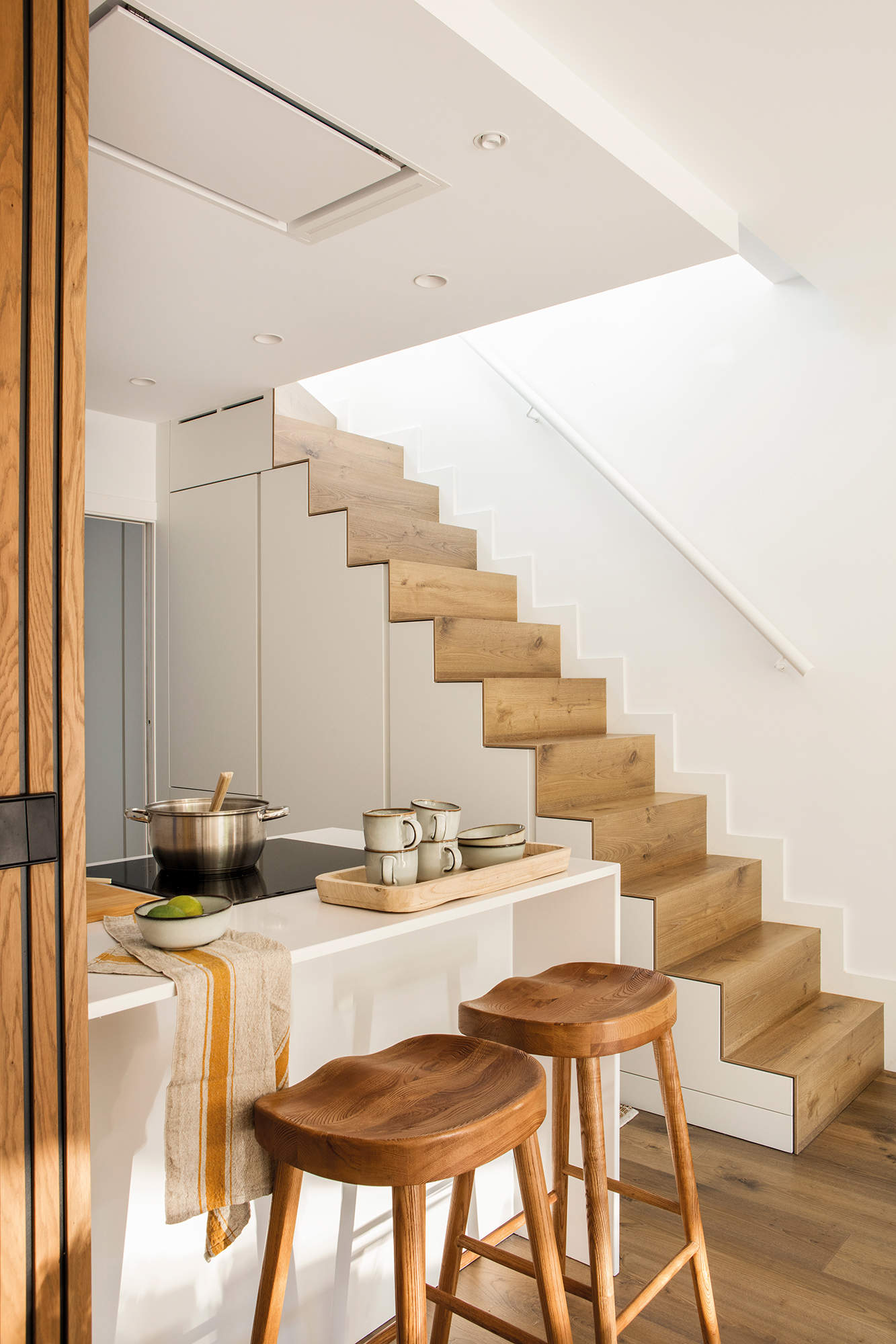 Cocina en blanco y madera con armarios en la escalera. 