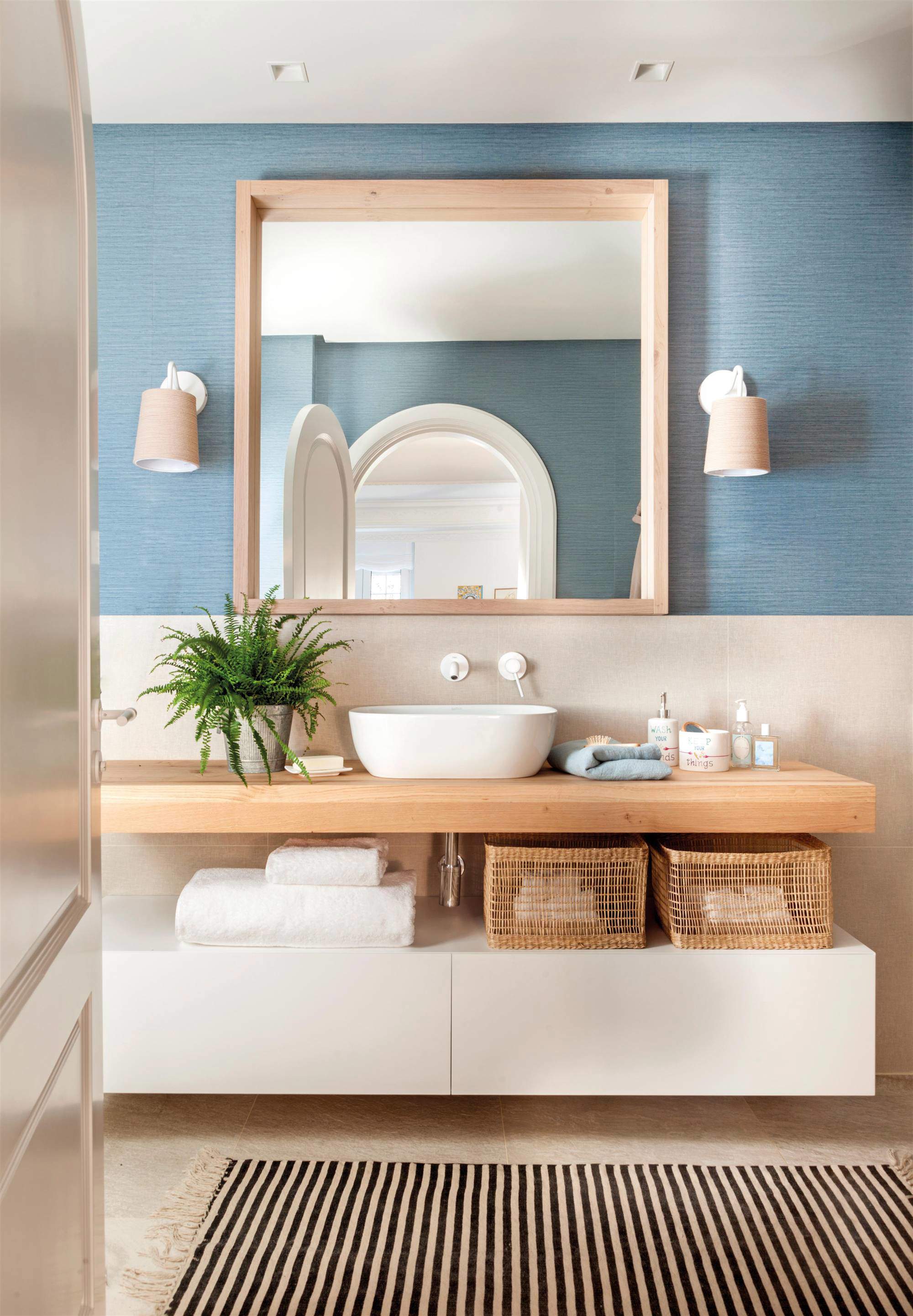Baño con frente de papel pintado azul con textura y mueble volado en blanco y madera.