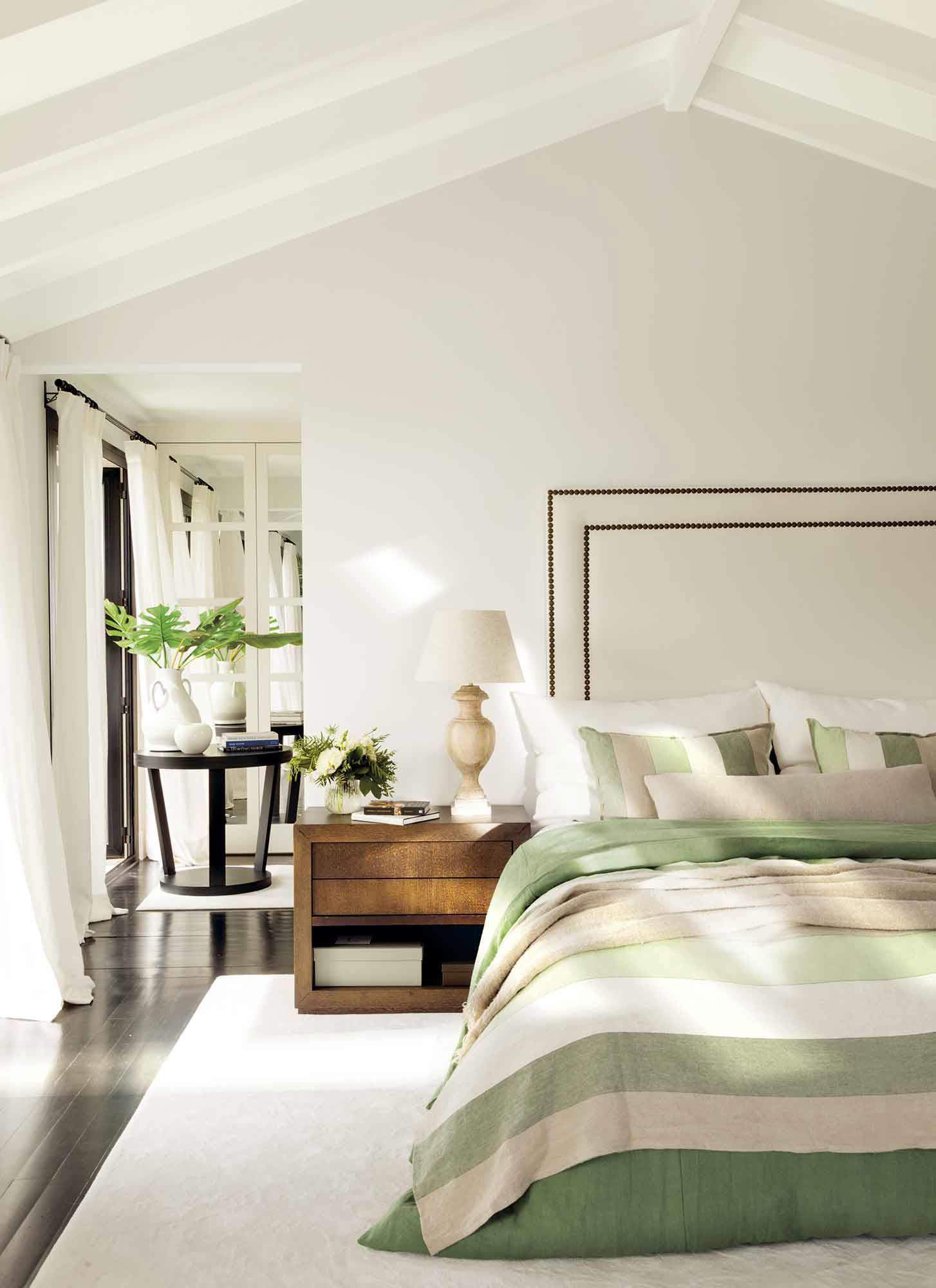 Dormitorio con techo abuhardillado en blanco, ropa de cama en tonos verdes a juego con arreglos florales.